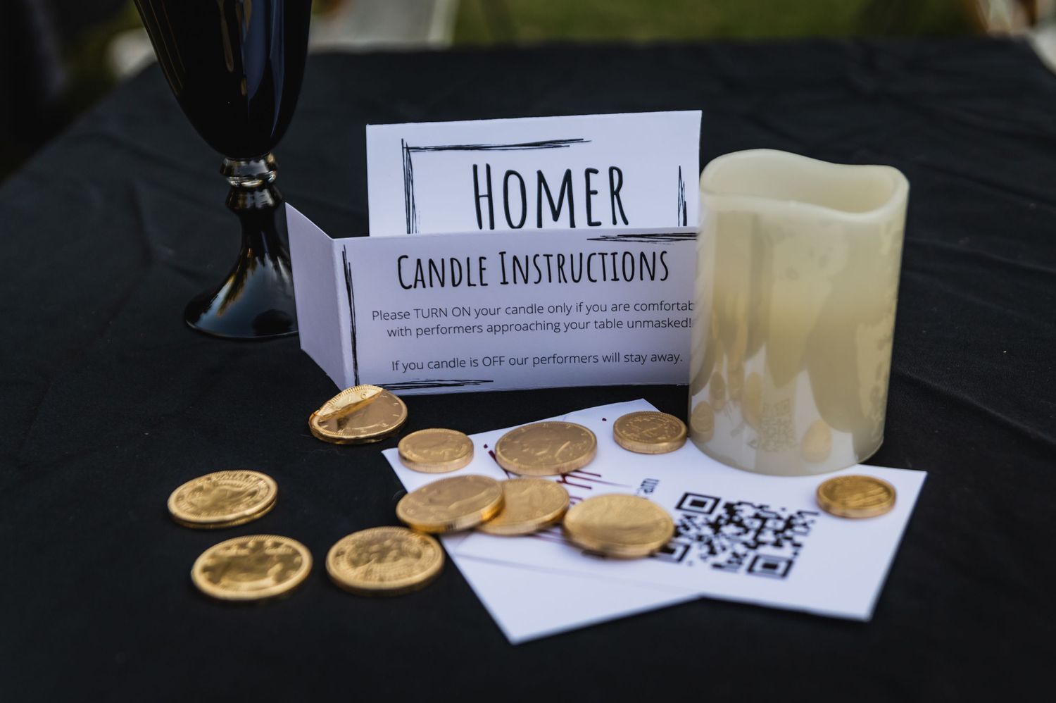 Table display featuring Homer candle instructions and gold coins with QR codes.