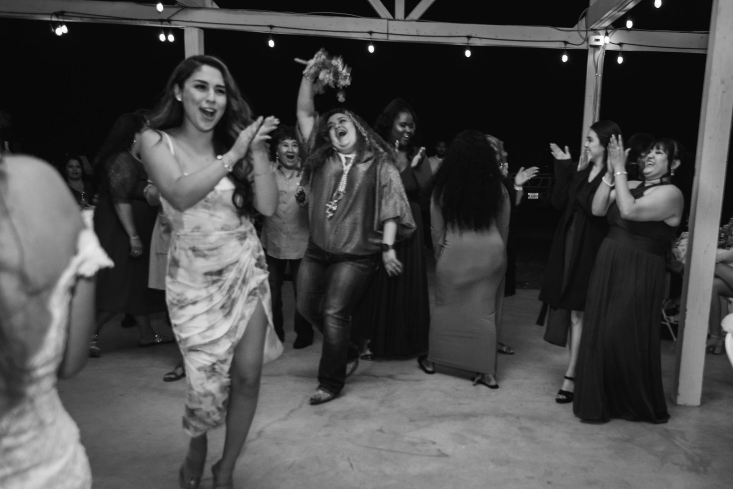 Wedding guests dancing and celebrating in a rustic barn venue at night.