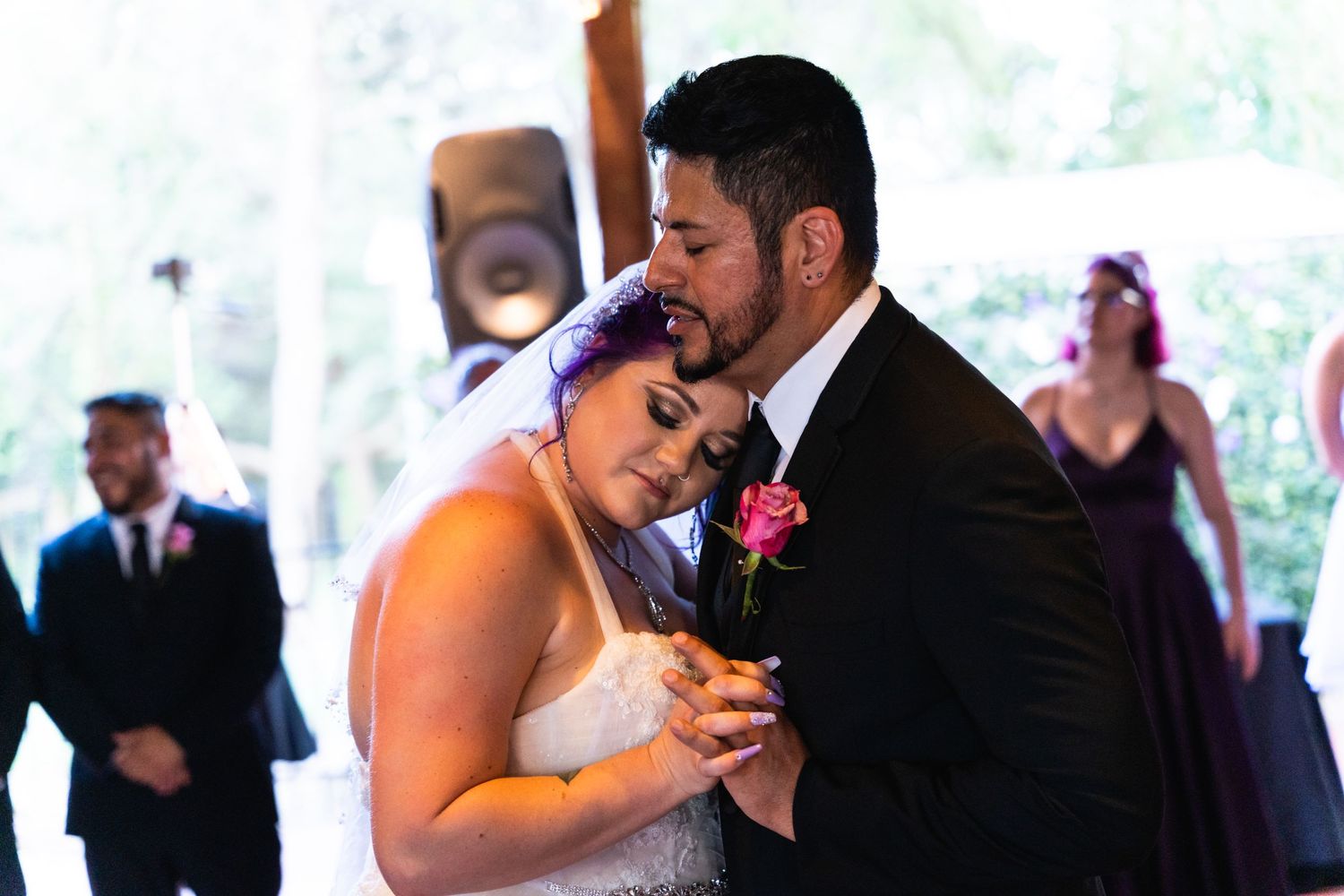 A tender slow dance moment at a wedding reception with a pink floral boutonniere.
