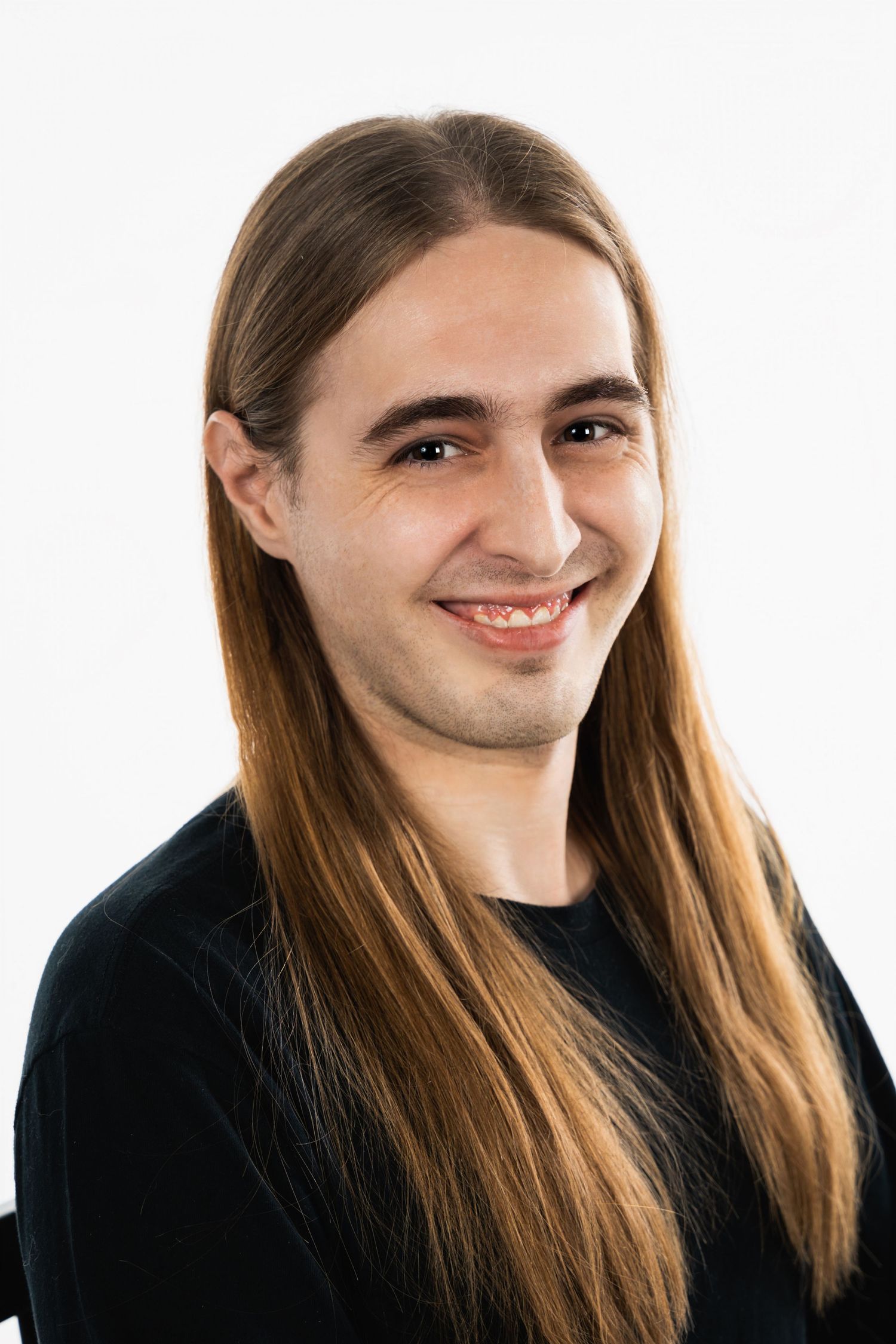 Person with long brown hair wearing black sweater against white background.