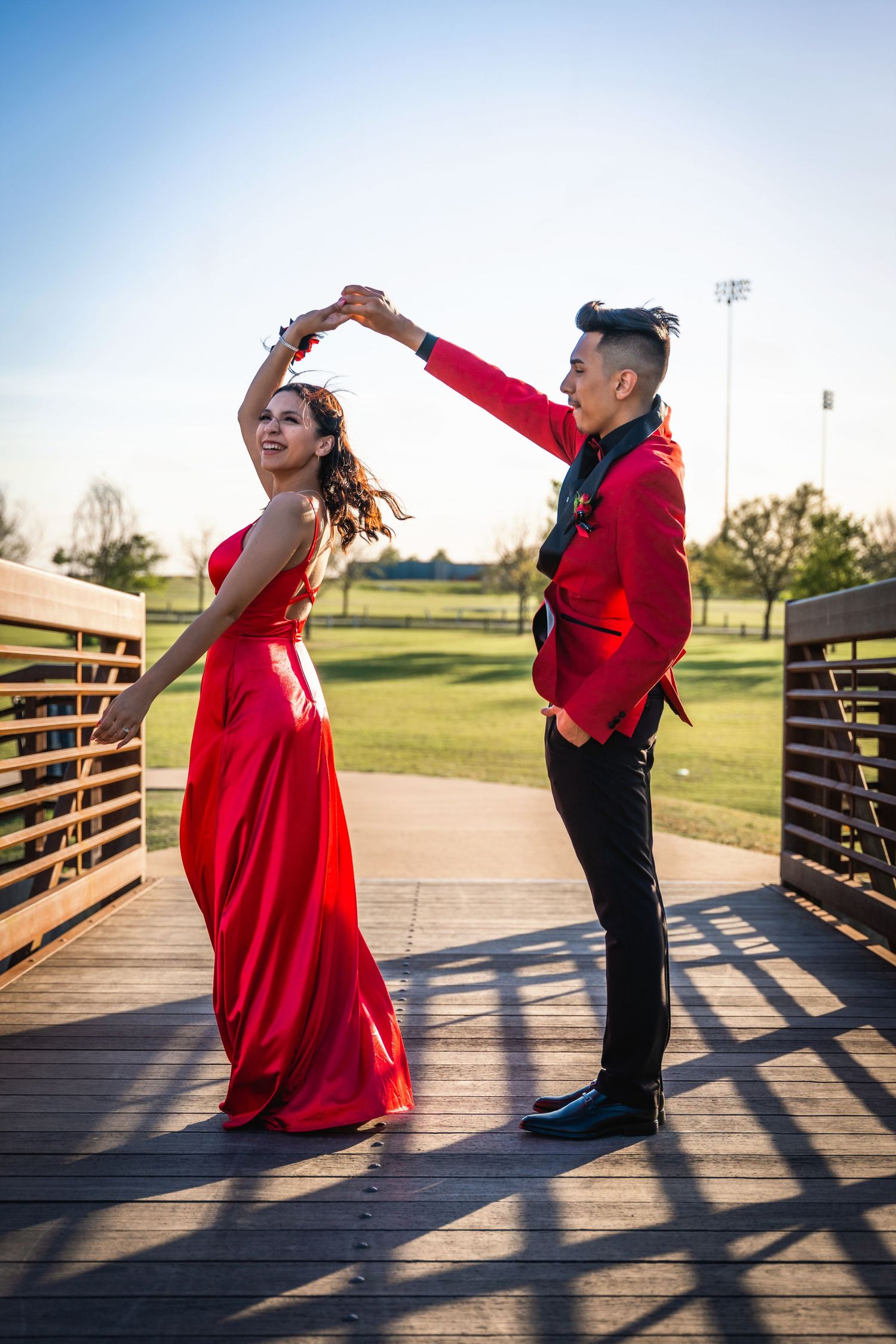 Couple in formal wear dancing on a wooden bridge, with the woman in a flowing red dress.