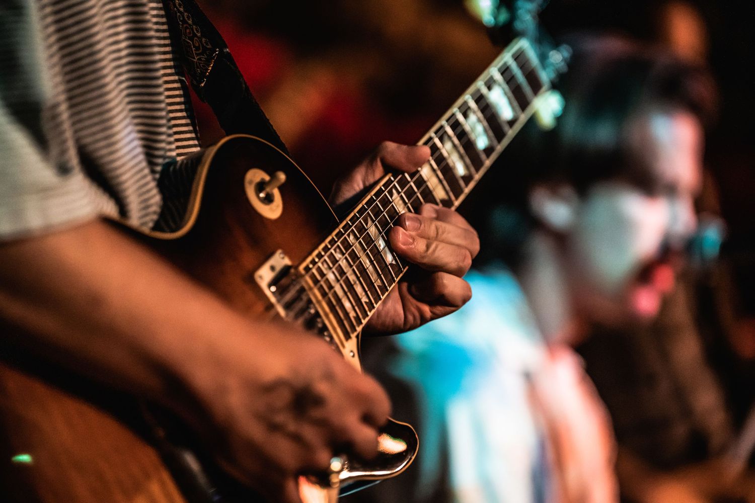 Close-up shot of hands playing an electric guitar with warm stage lighting.