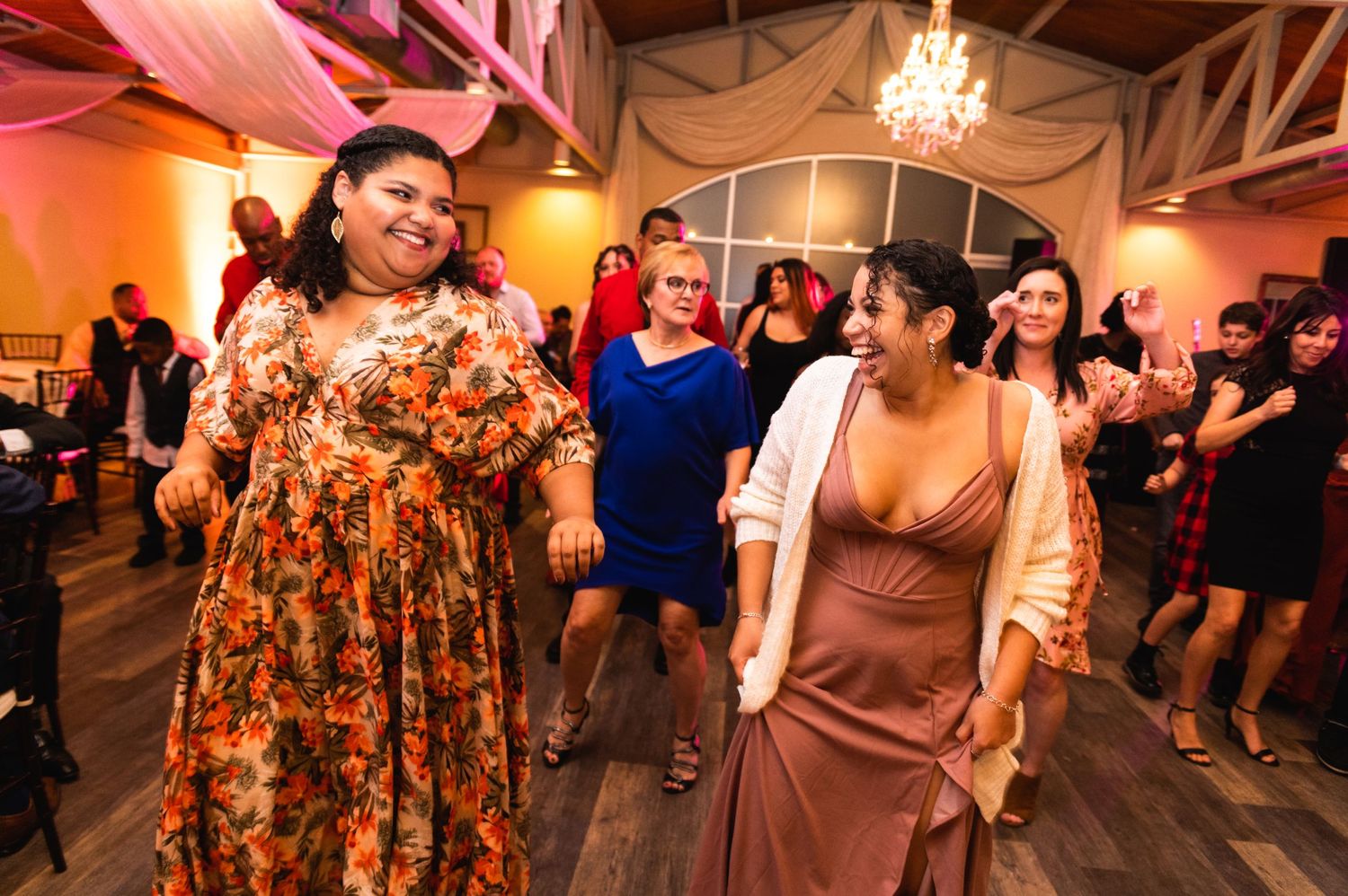Wedding guests dance and celebrate in colorful attire at a lively indoor reception.
