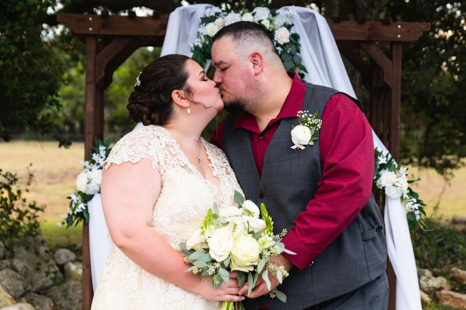 Tender moment shared between newlyweds under floral arch with white bouquet.