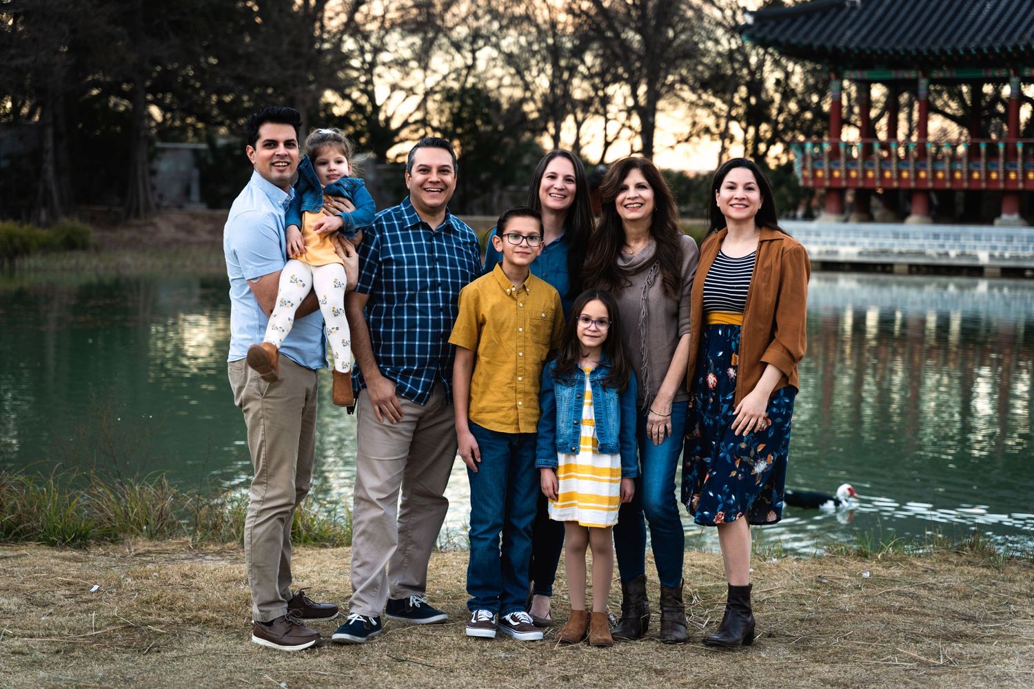 A family group poses together by a serene lake with a pagoda-style structure in the background.