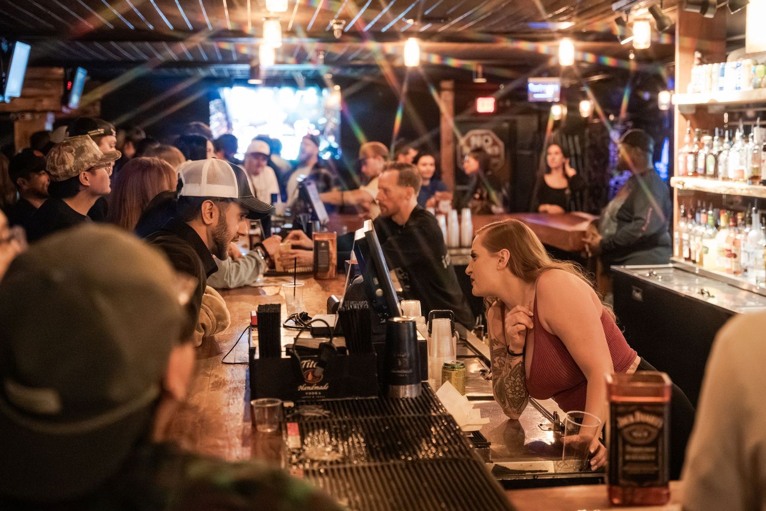 A crowded bar interior with wooden decor and warm lighting shows patrons seated at the counter during evening service.