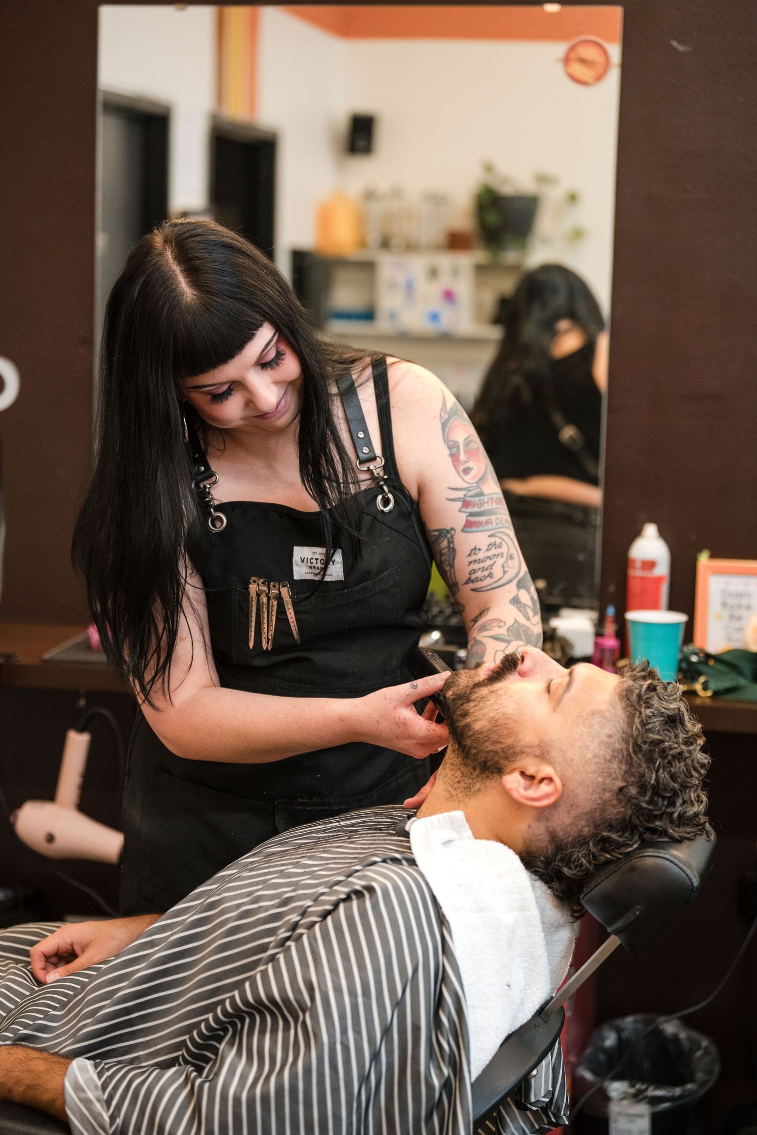 A barber applies shaving cream and performs a traditional straight razor shave on a client in a barbershop.