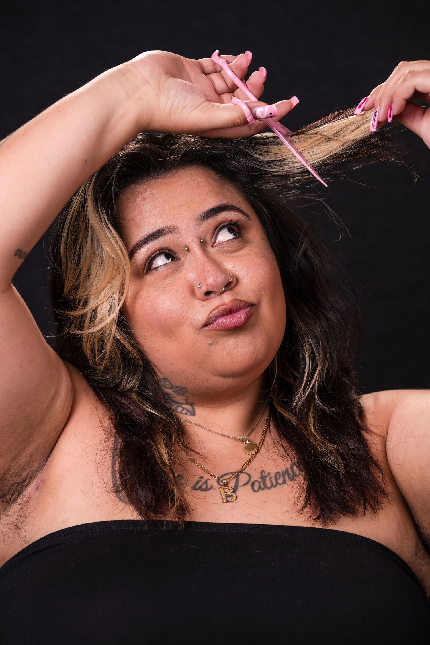 A woman with dark hair makes silly faces while trimming her bangs with pink scissors against a black background.