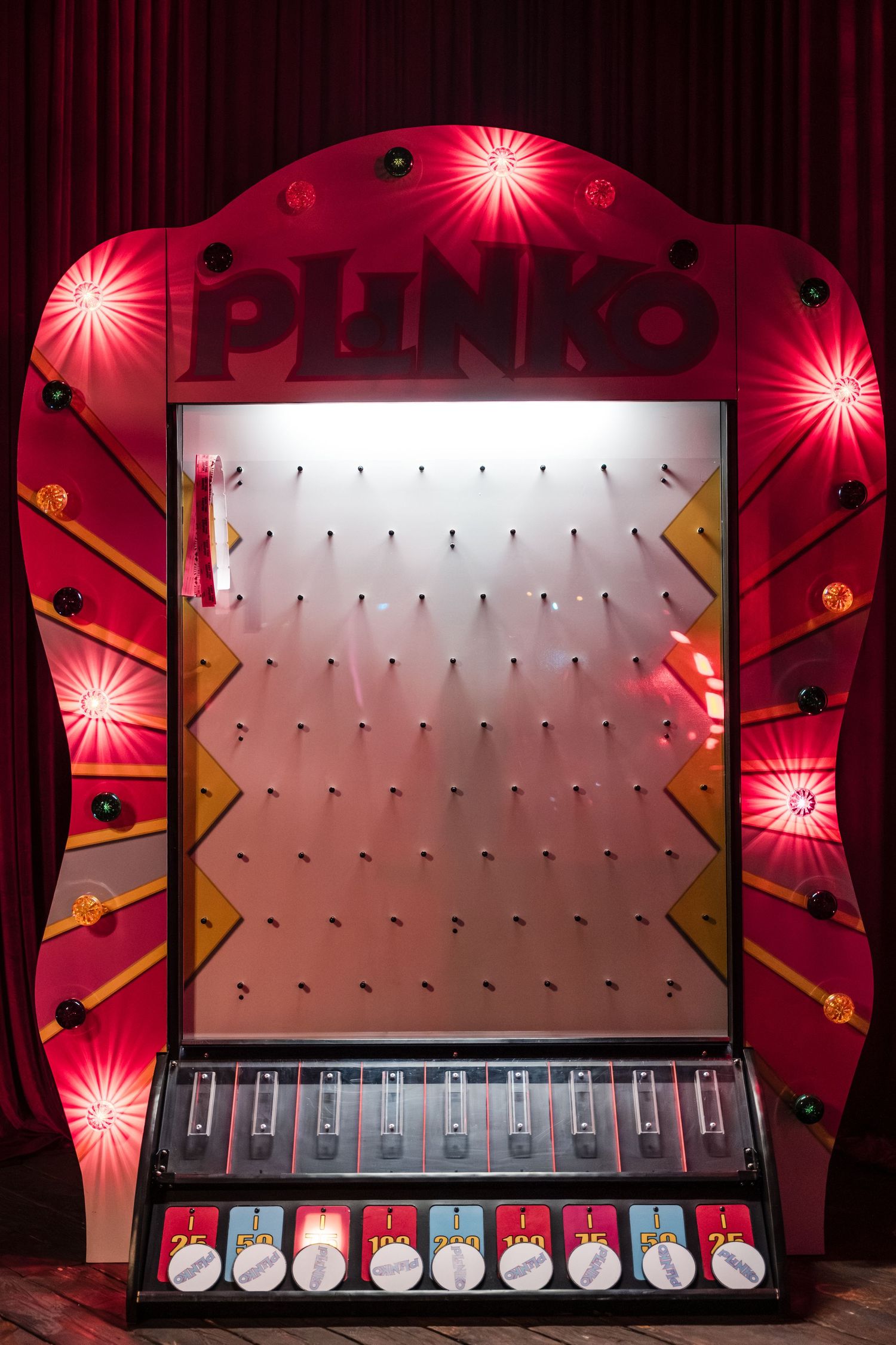 A pink and red illuminated stage backdrop with geometric patterns and glowing lights creates a dramatic performance space.