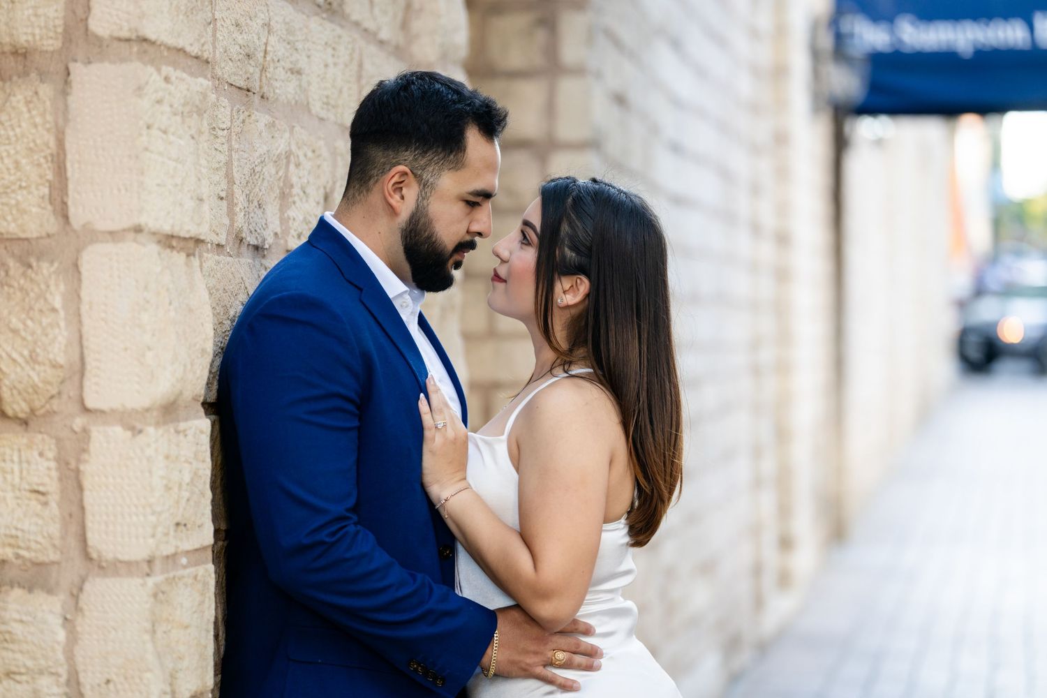 A couple shares an intimate moment against a stone wall background in formal attire.