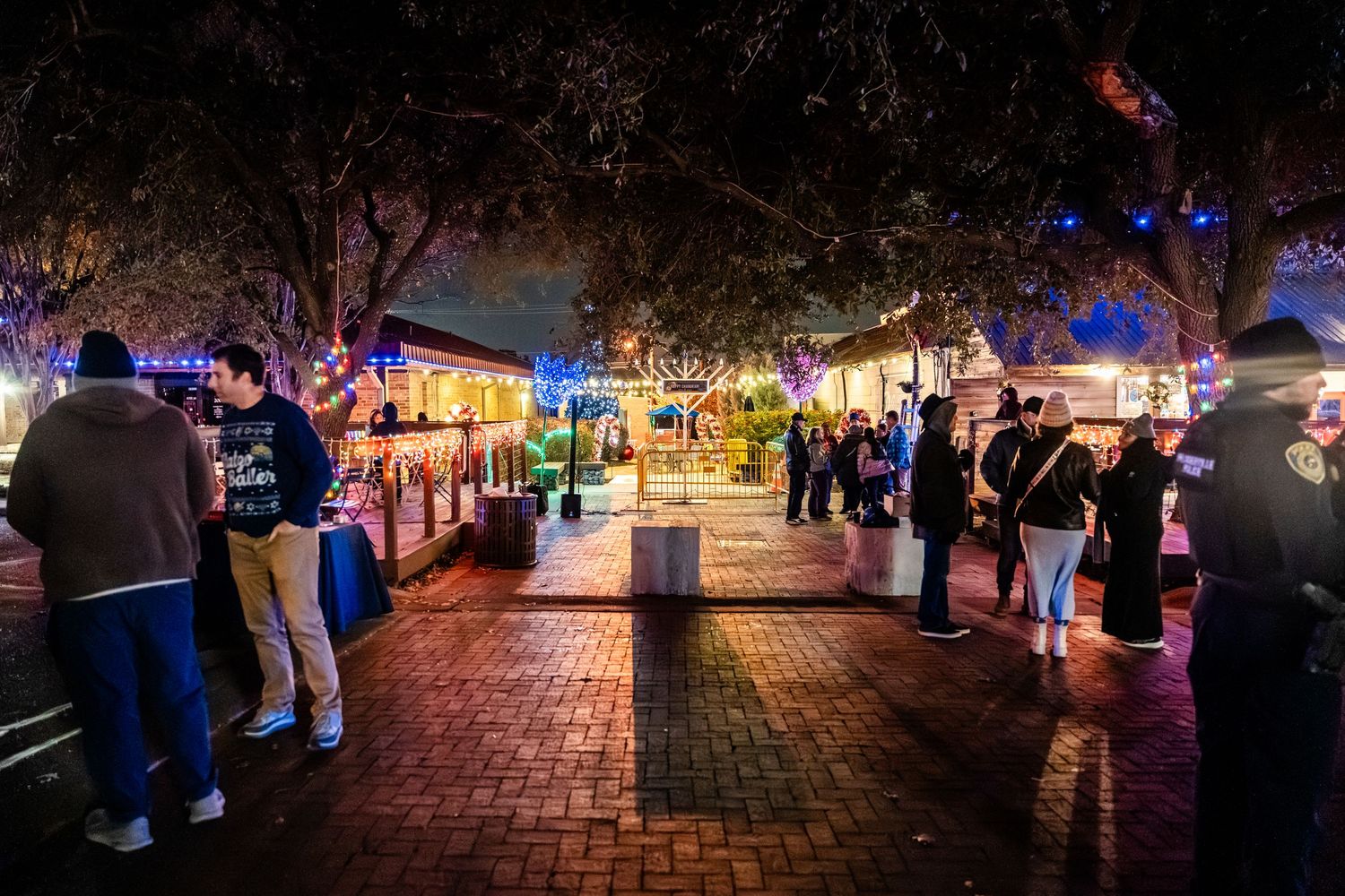 Nighttime view of a brick-paved street with colorful lights and people browsing outdoor market stalls in Florida.