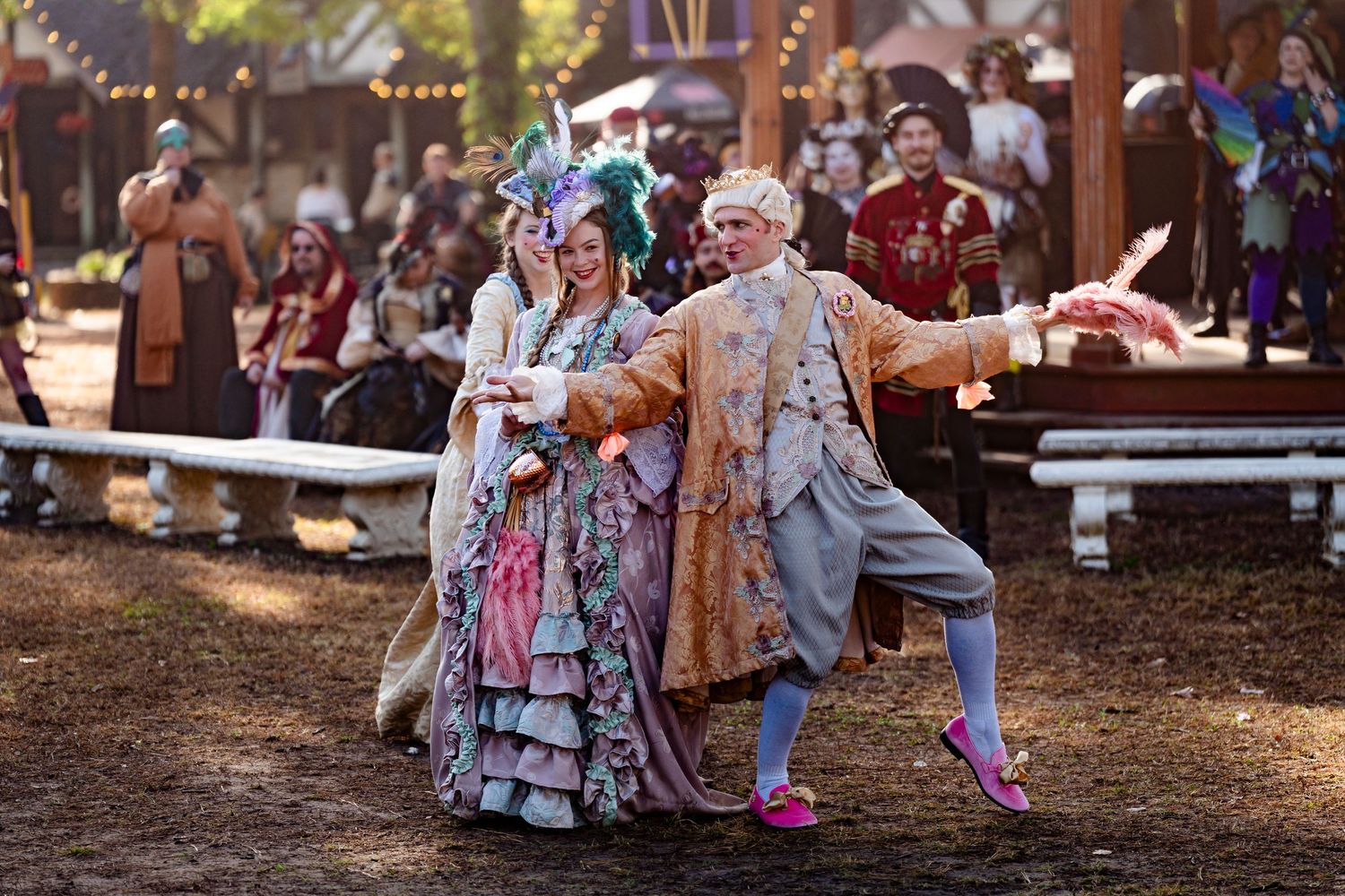 Dancers perform traditional folk dances at a festive outdoor gathering with string lights and decorations.