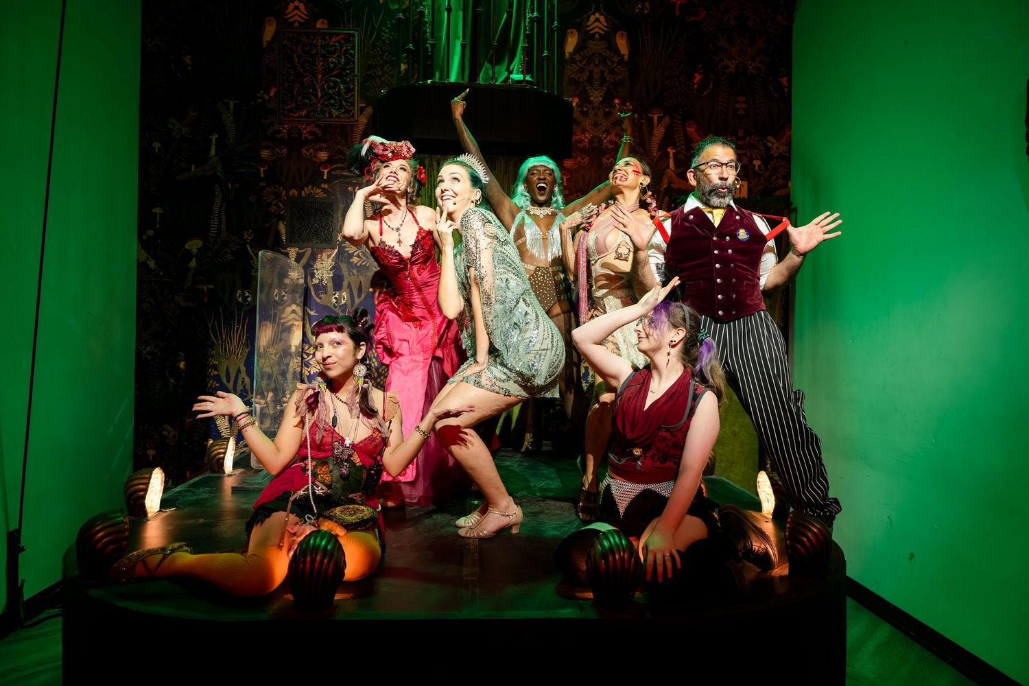 A theatrical performance with dancers in colorful costumes on stage under dramatic green lighting.