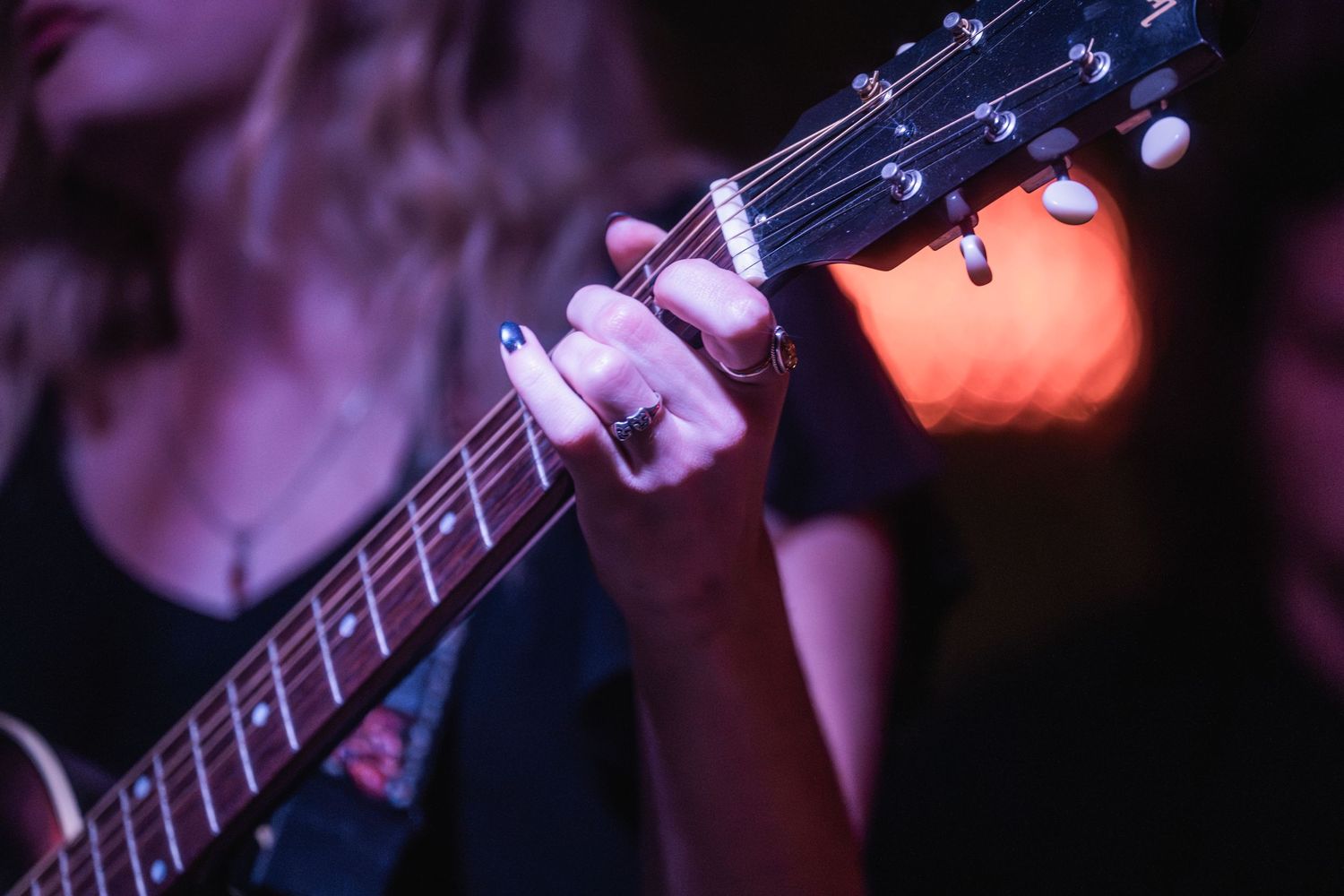 Close-up shot of hands playing an electric bass guitar on a dark stage with purple lighting.