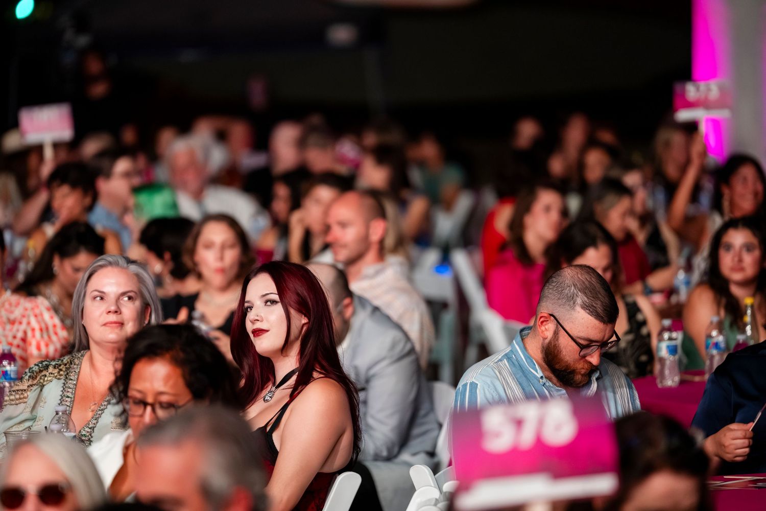 A large crowd of people gathered at an indoor event with colorful lighting and festive atmosphere.