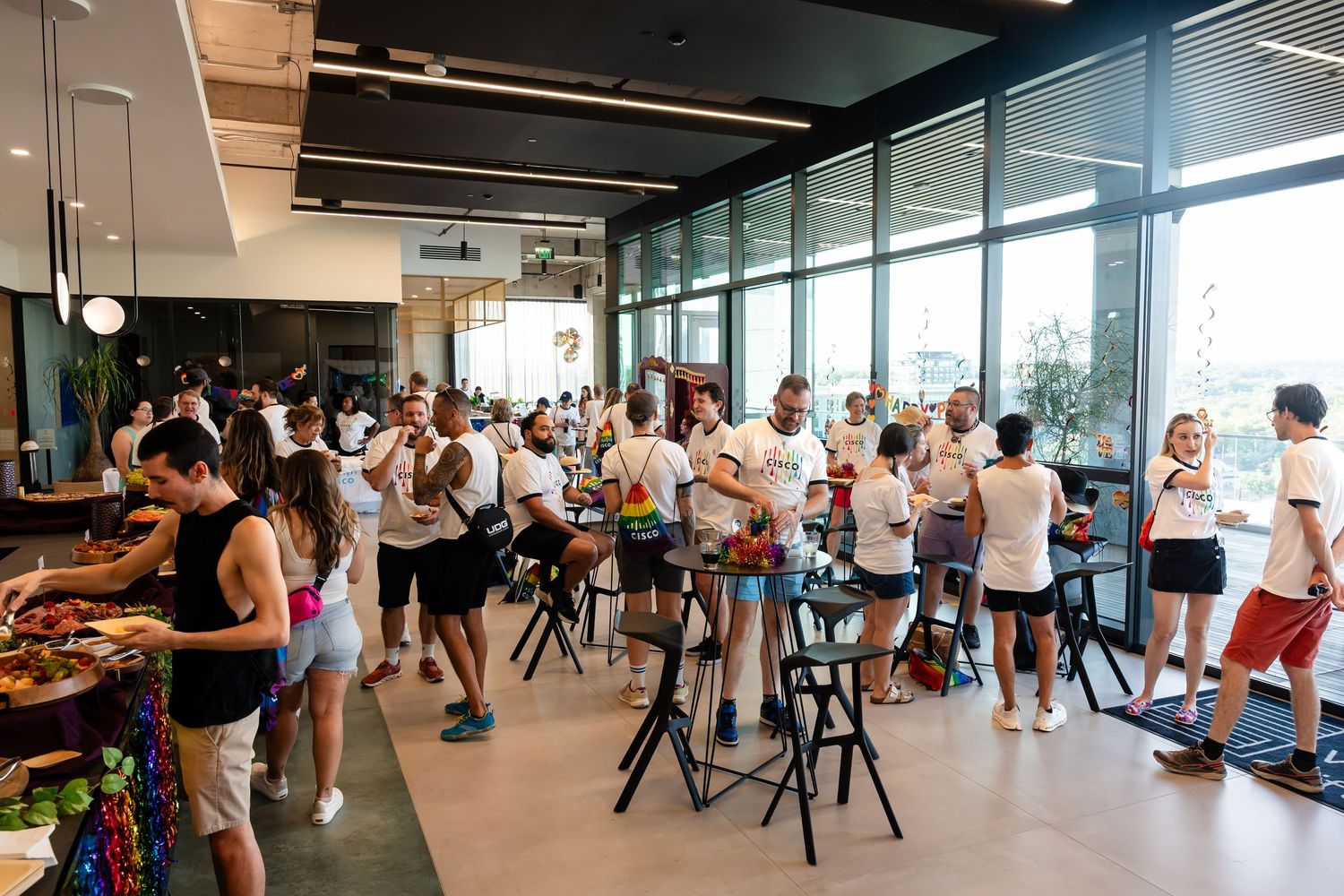 Diverse group of people socializing at a modern office party with large windows and casual attire.