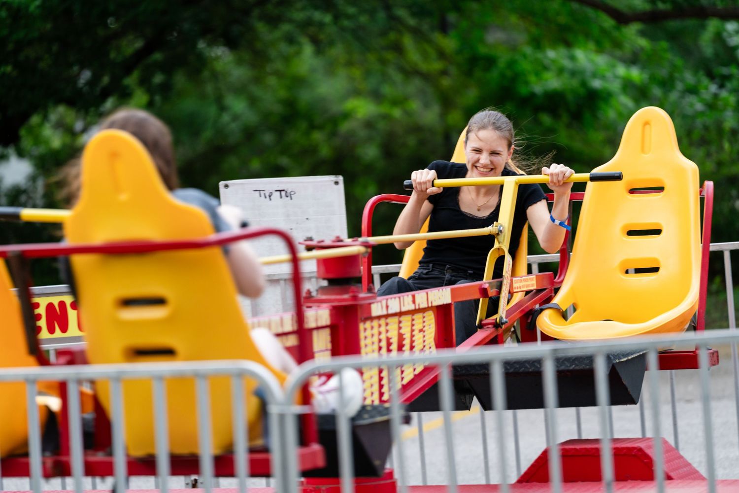 A smiling young woman enjoys a yellow carnival ride at an outdoor amusement park or fair.