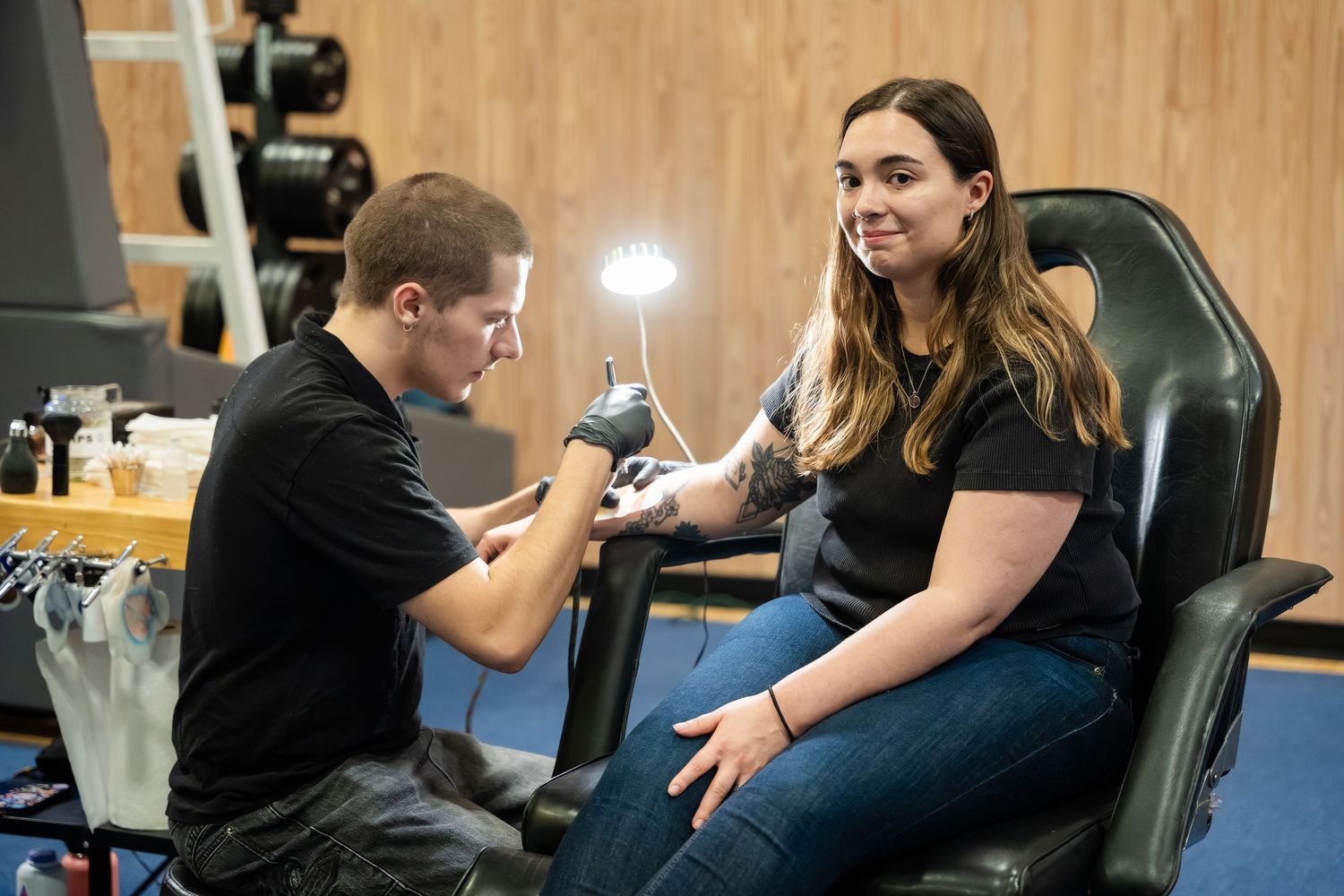 Tattoo artist applying a tattoo on a young woman's arm in a modern tattoo studio with professional lighting.