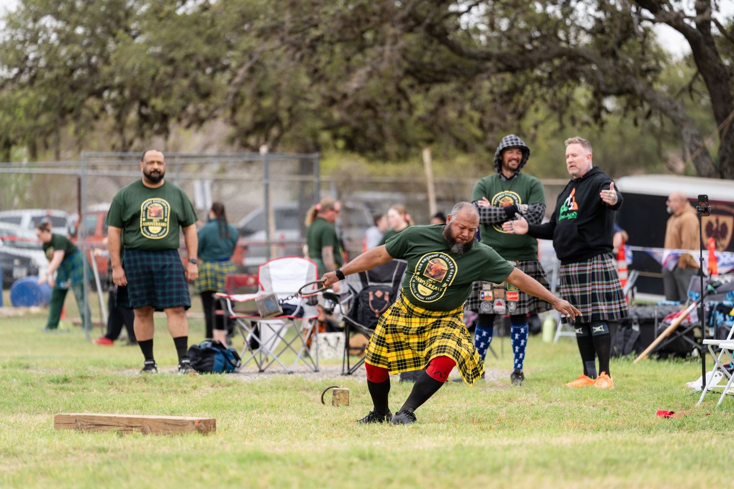 Men in kilts compete in Highland Games athletic events on a grassy field, throwing heavy objects in traditional Scottish competition.