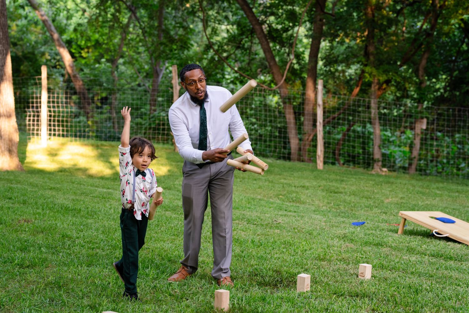 Man and child playing Kubb lawn game outdoors on green grass in a backyard setting.
