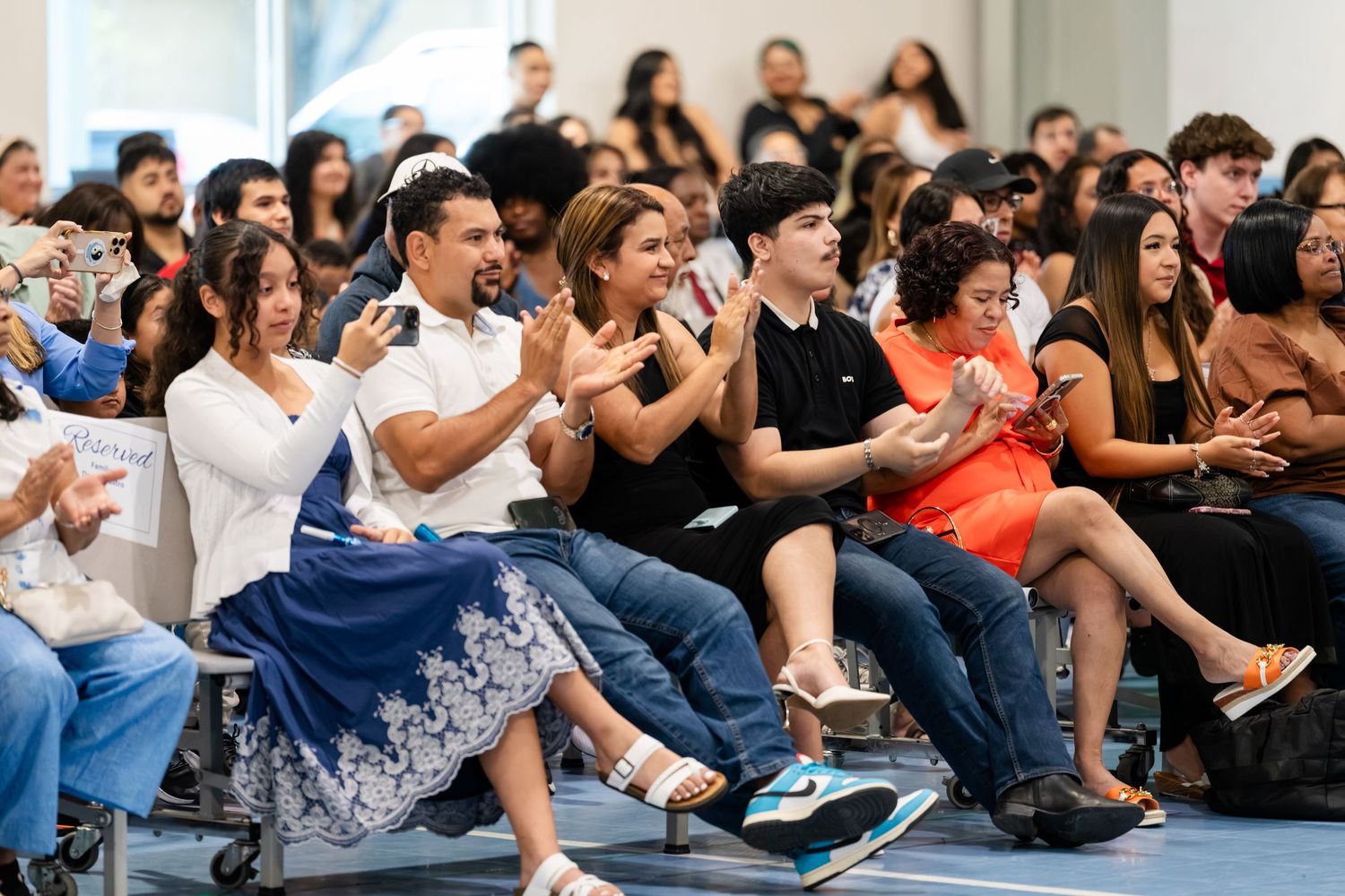 Diverse audience clapping and smiling at an indoor event, seated in rows during a celebration or ceremony.