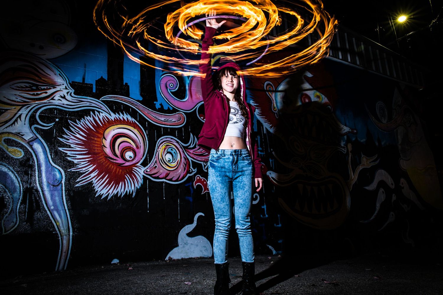 Light painting photography against colorful graffiti wall creates spiral light trails in dark urban setting.