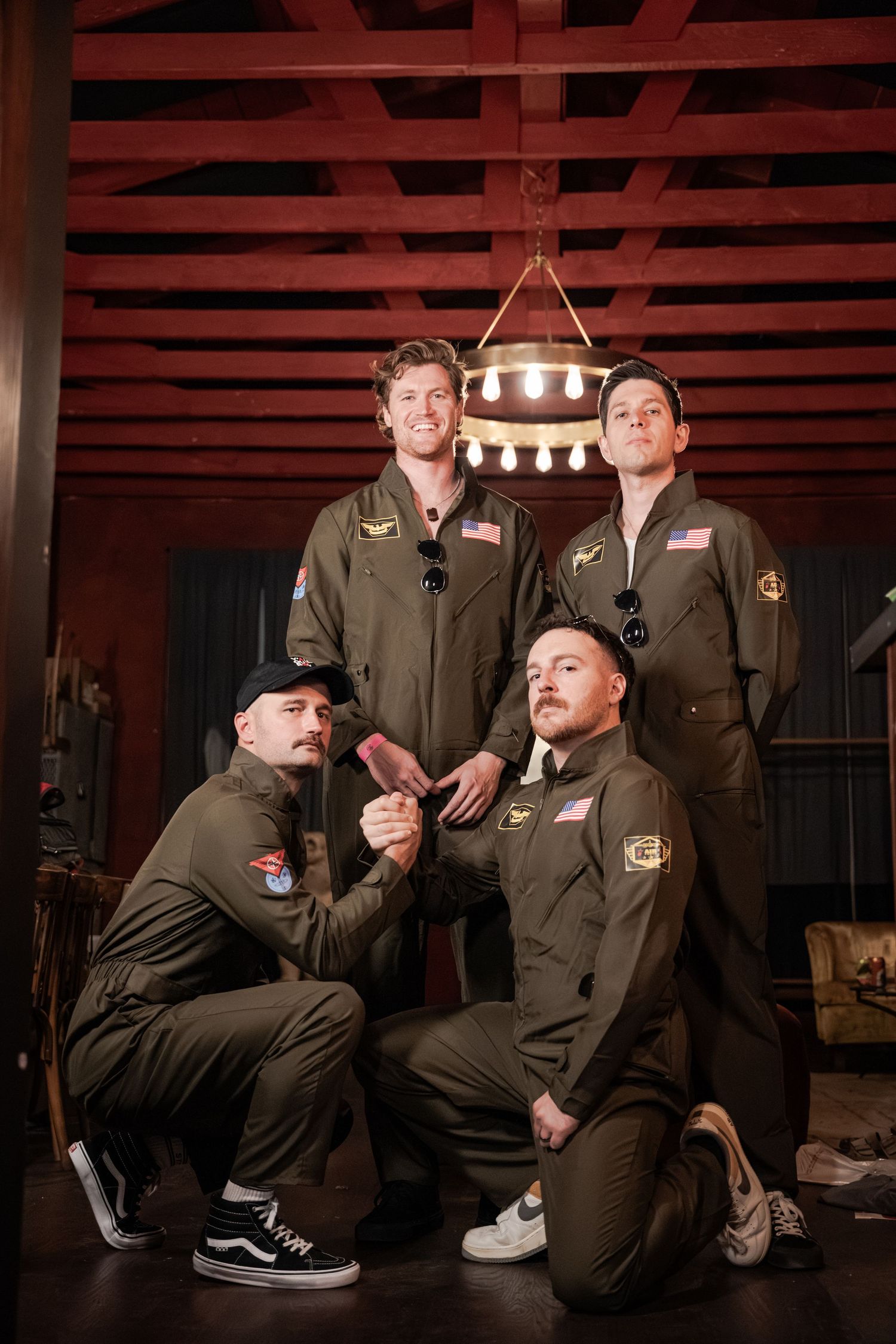 A group in matching workwear uniforms sits casually on wooden steps in a dimly lit industrial setting.