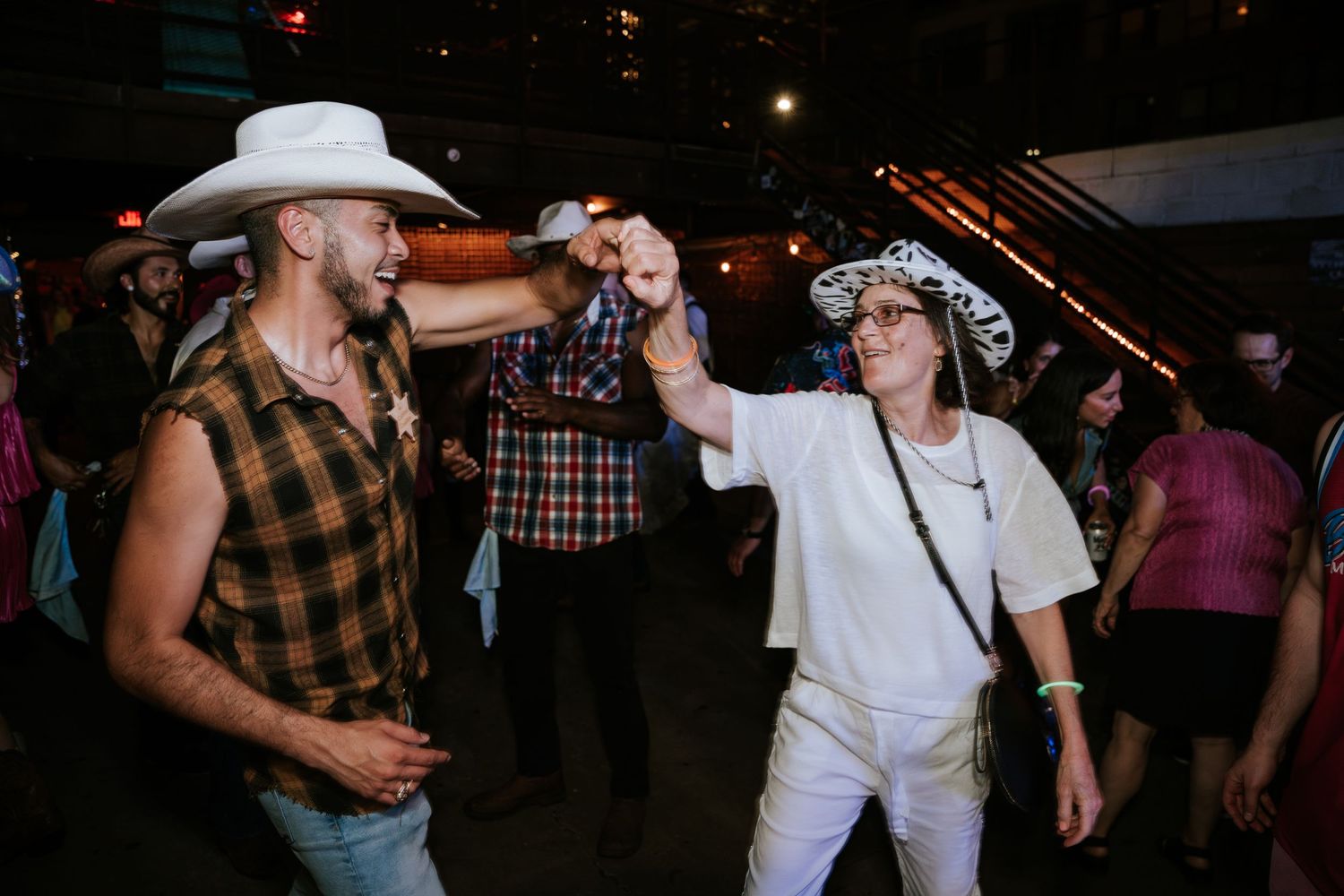 Party guests in cowboy hats dance and celebrate at a western-themed event.