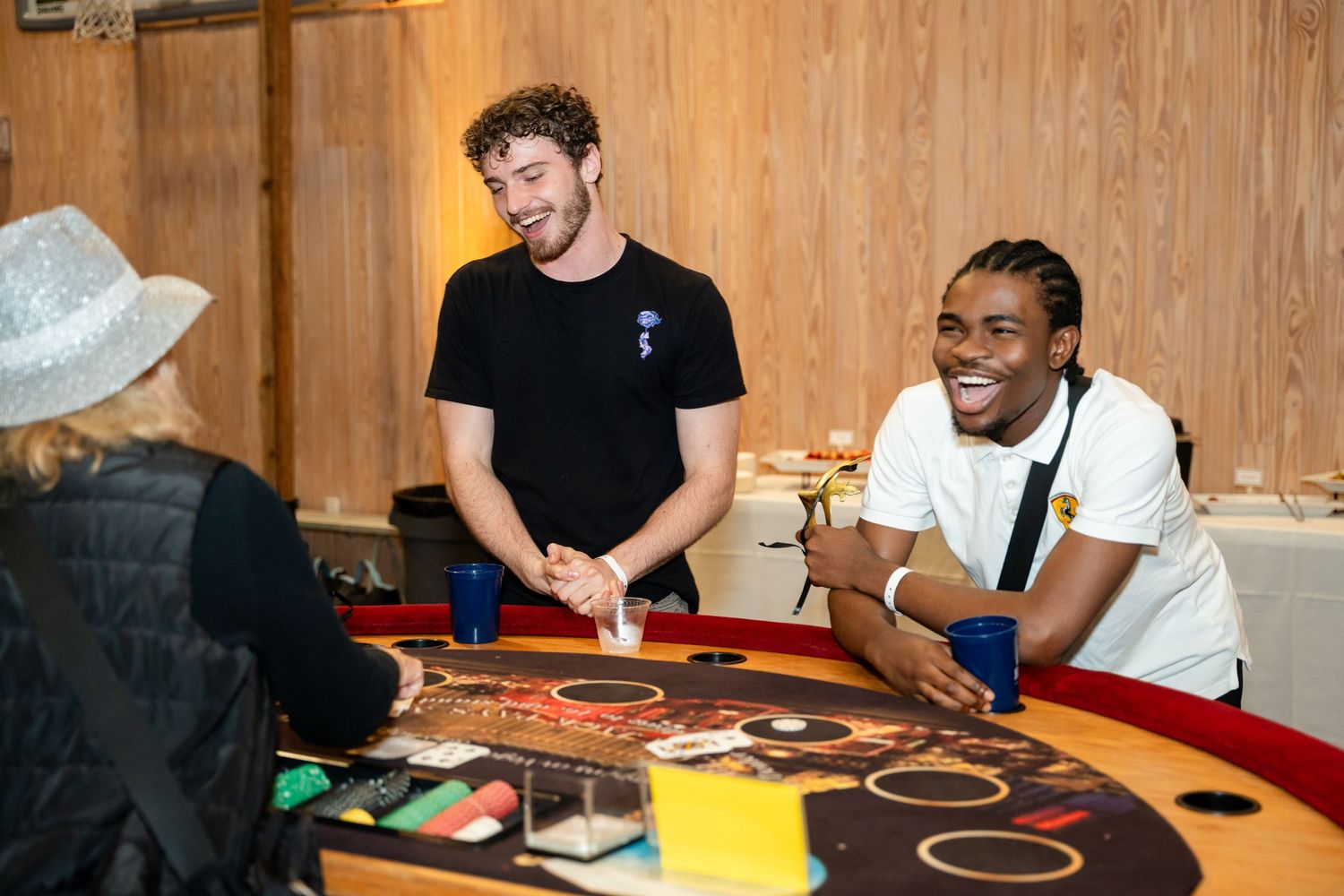 Dealers and players interact around a red curved gaming table at an indoor casino event.