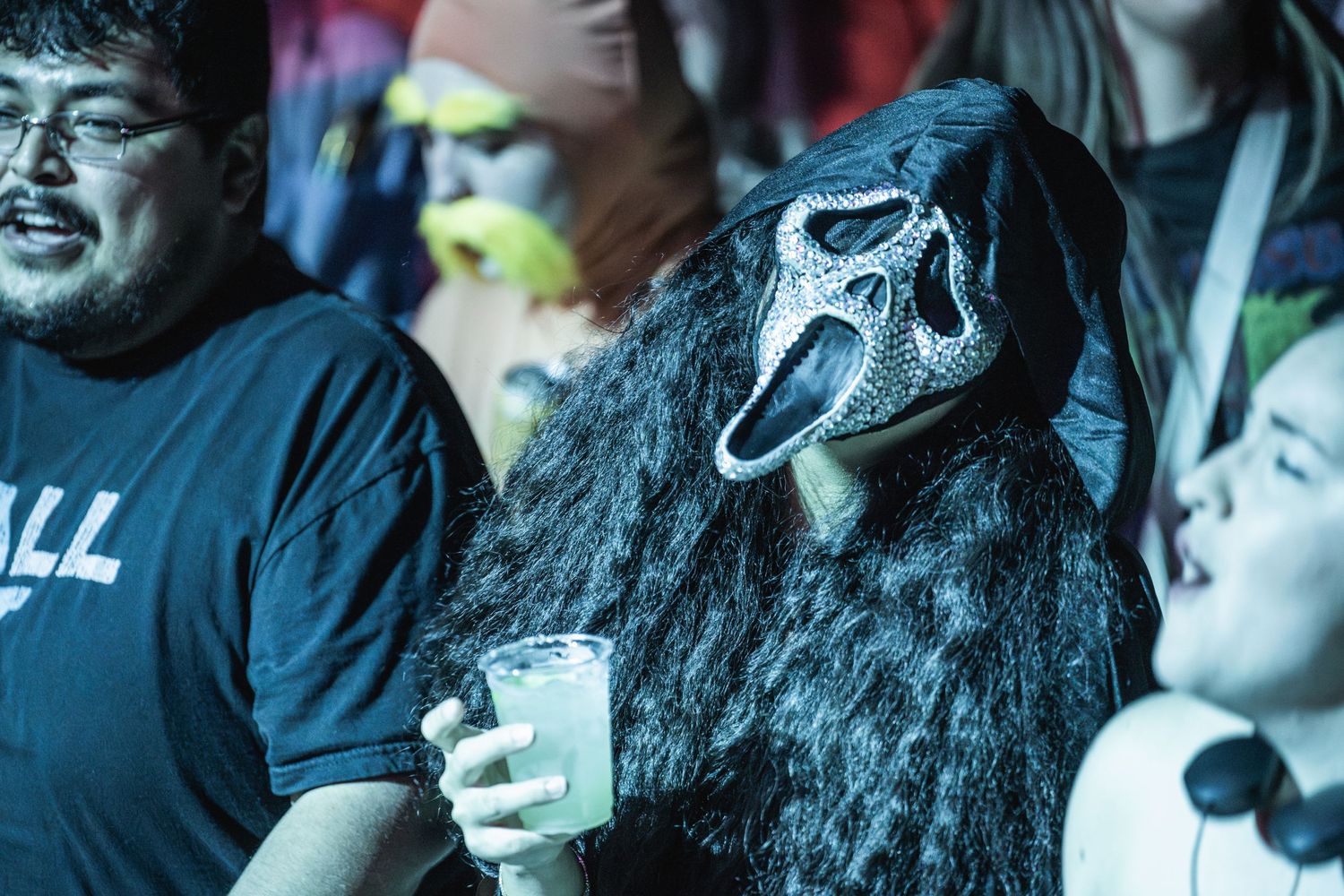 Concert attendee wearing a spooky ghost mask holding a drink in the crowd.
