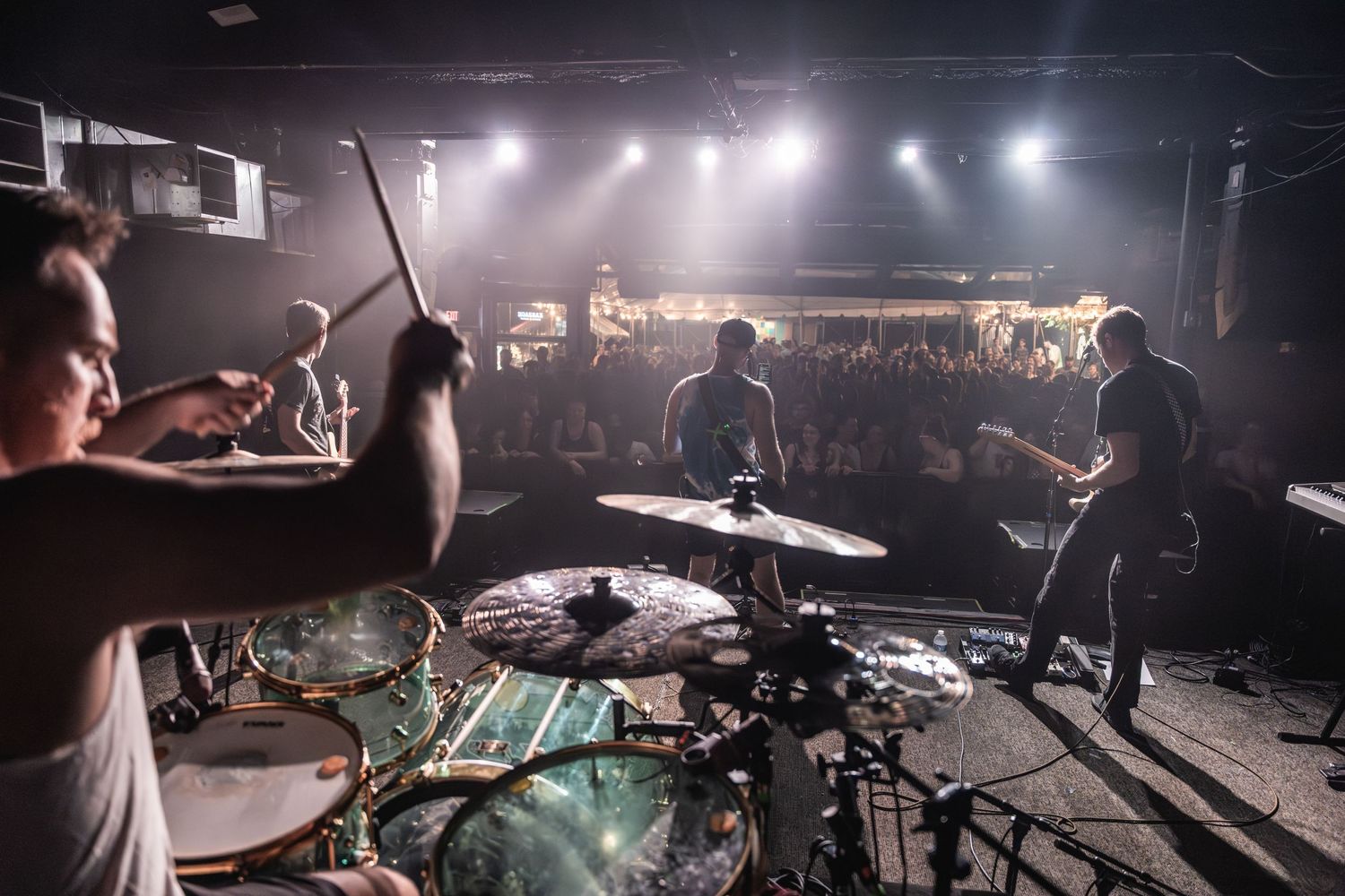 Wide shot of band performing on stage with silhouetted crowd visible in atmospheric lighting.