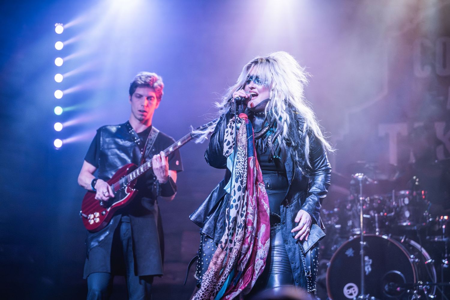Rock band performs energetically on stage with dramatic blue lighting and theatrical smoke effects.