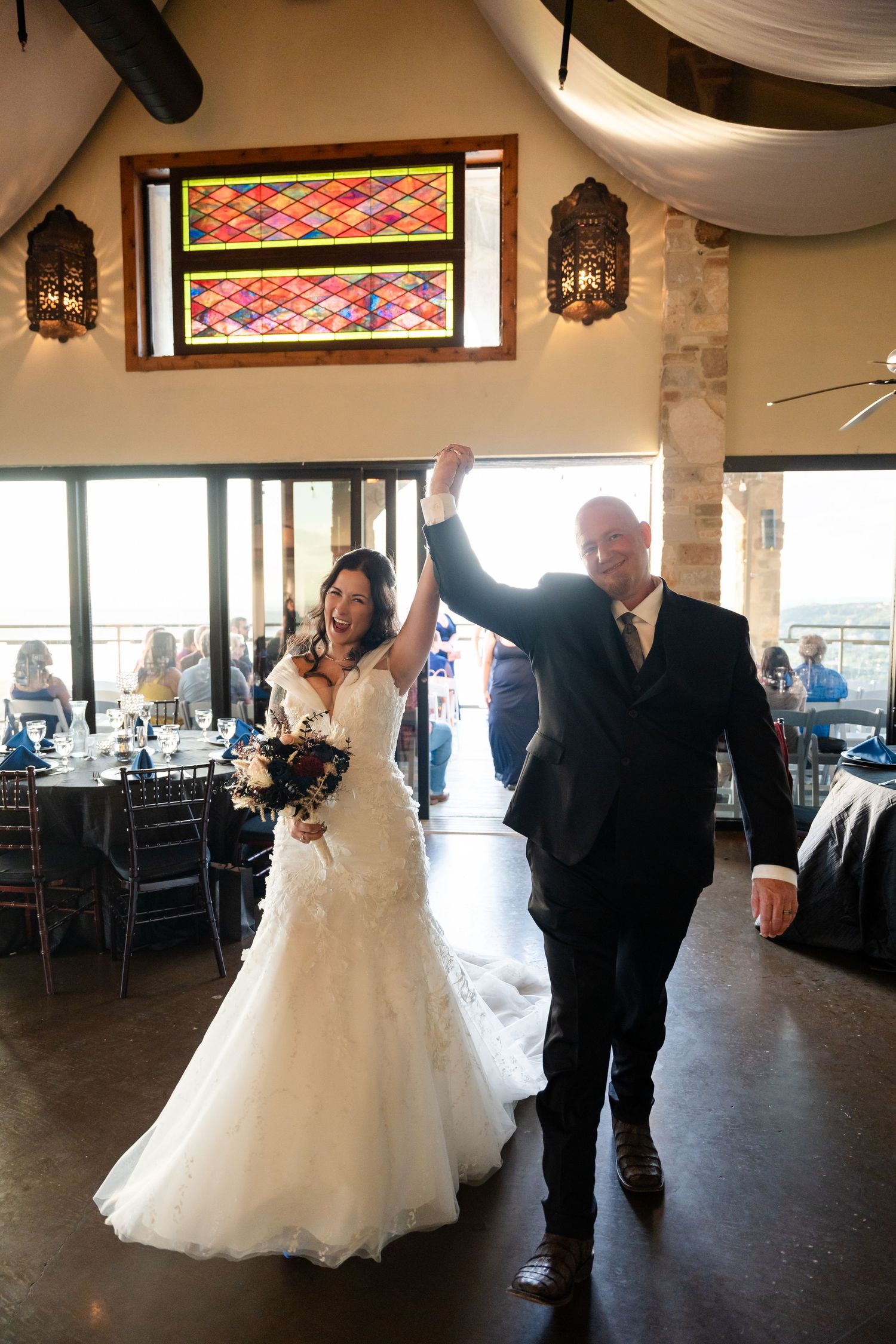 Newlyweds make grand entrance into reception hall with stained glass windows and lanterns.