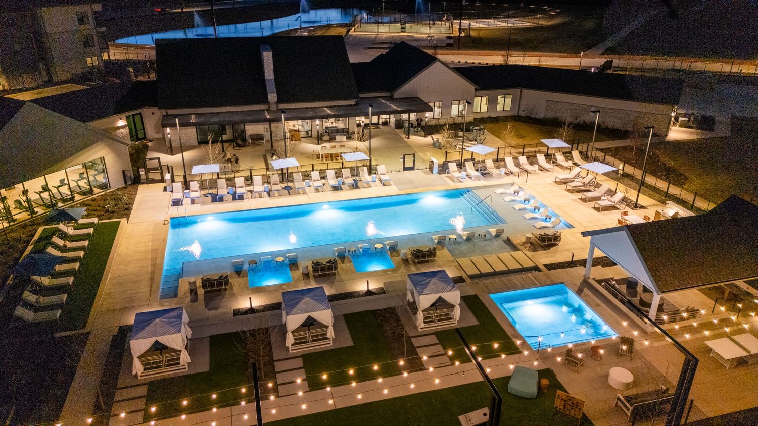 Aerial view of illuminated resort pools and cabanas at night with modern amenities and lounge areas.