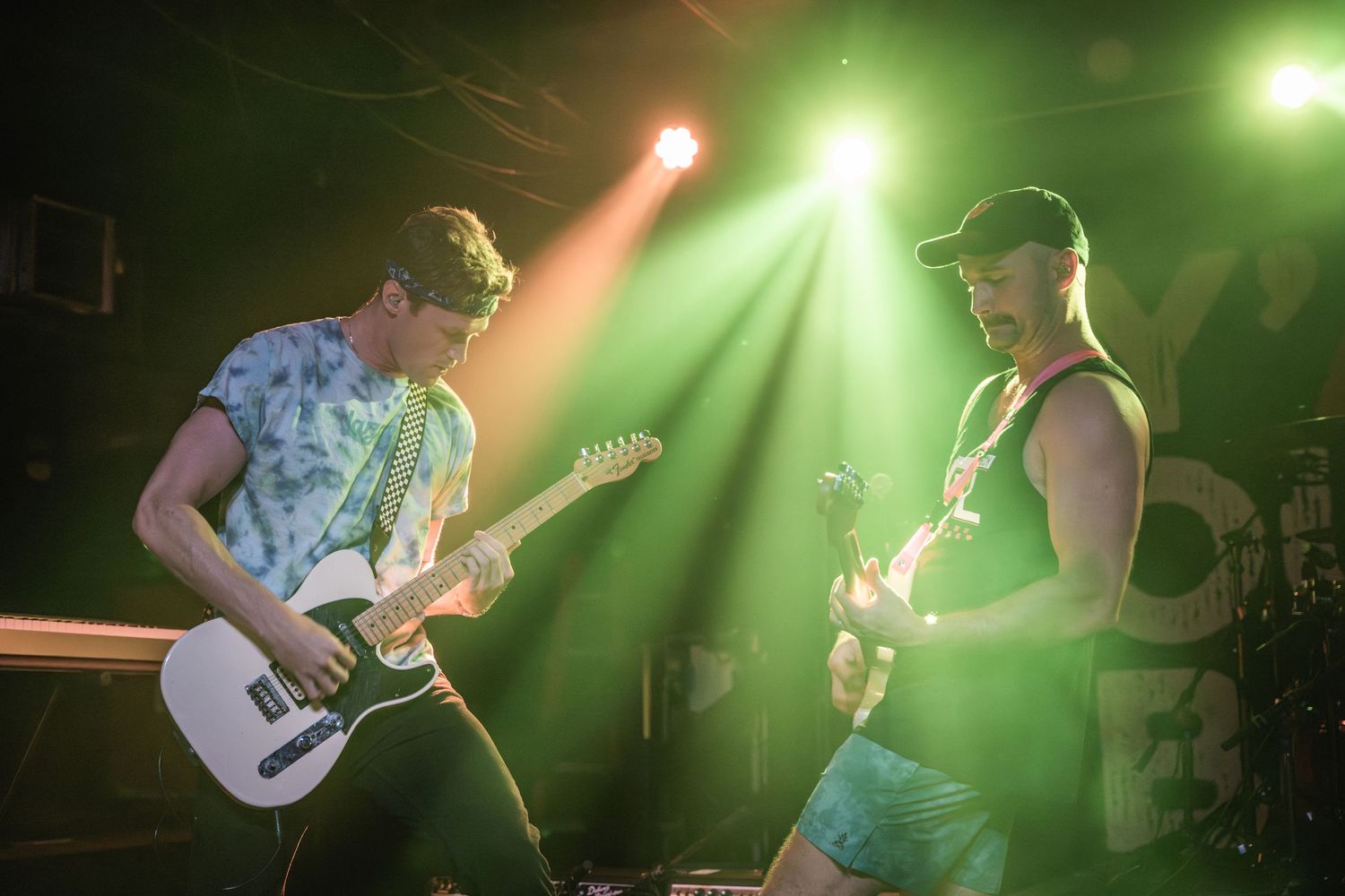 Two guitarists jamming together on stage under green spotlights.