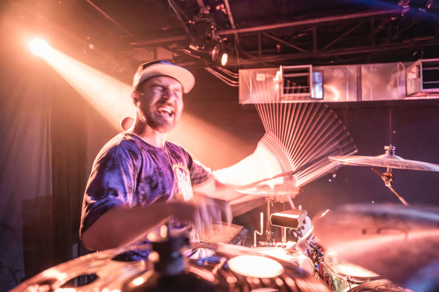 Drummer playing with orange stage lighting and motion blur effects.