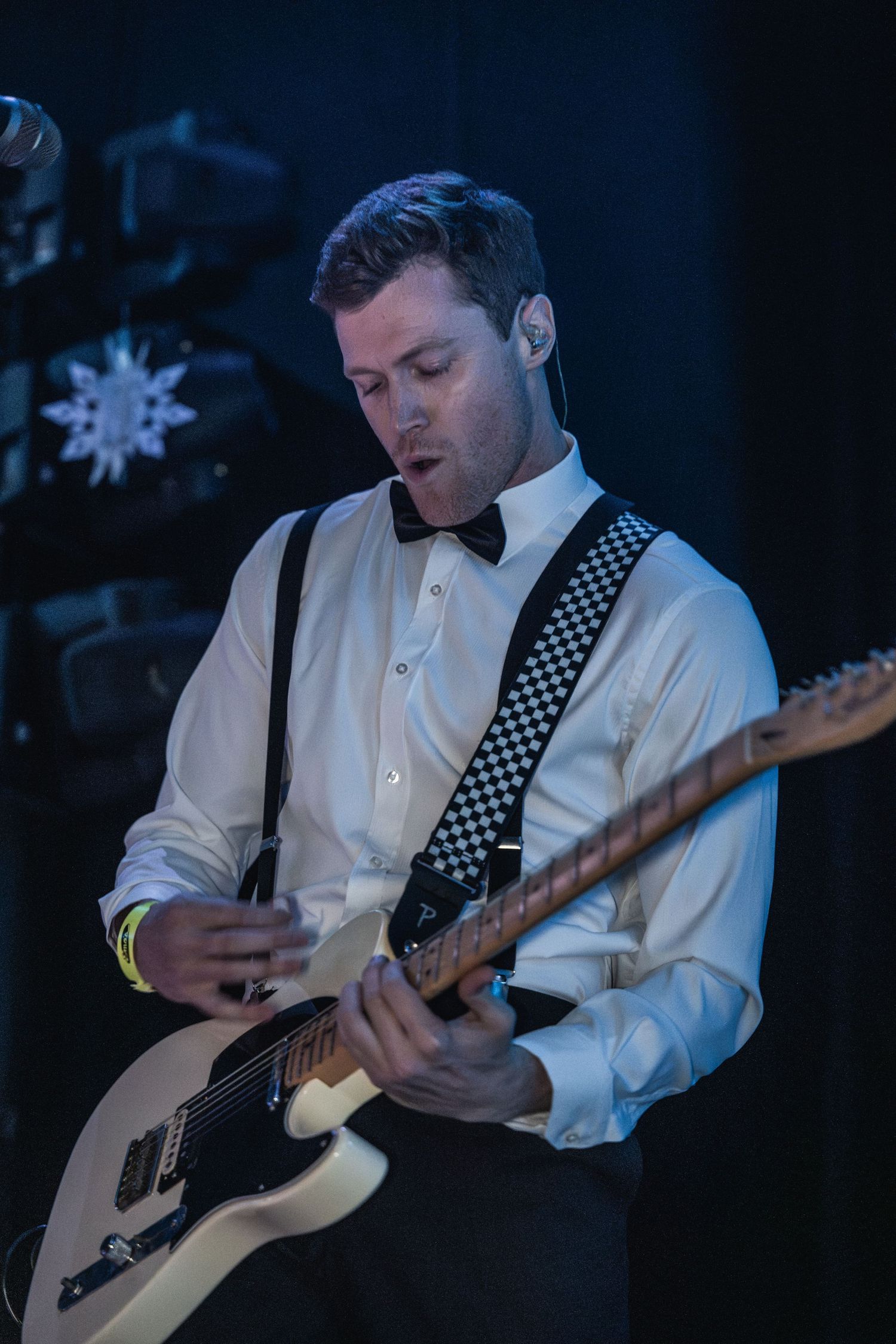 Guitarist in formal attire performs on stage with snowflake decorations.