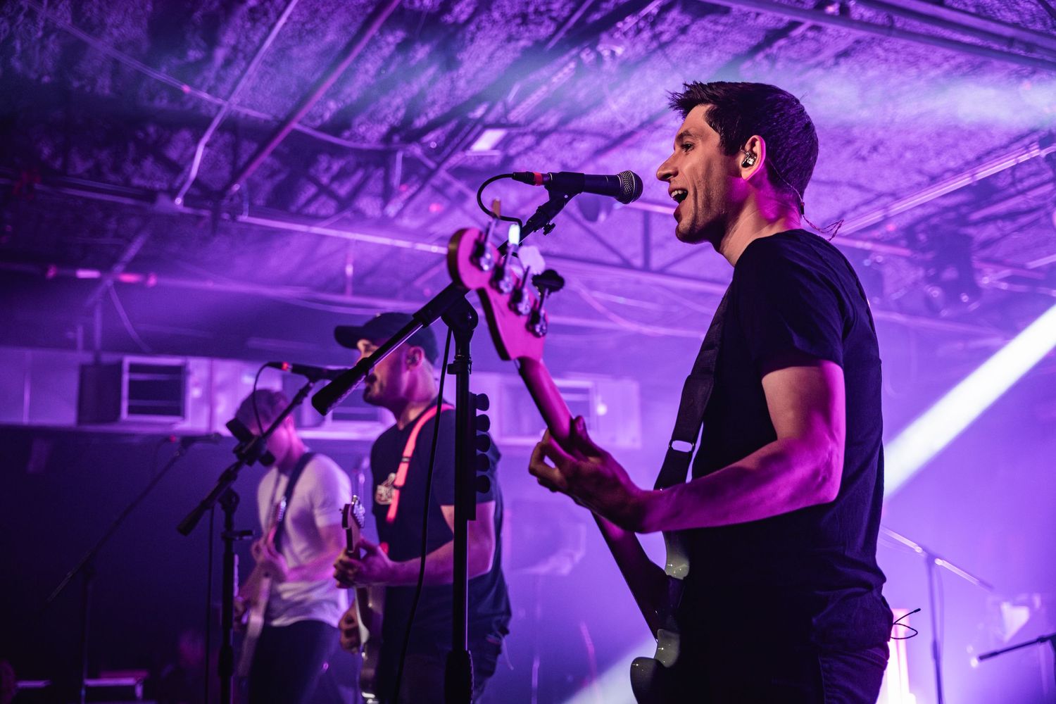 Concert performer playing guitar and singing into microphone under purple stage lighting during live music show.