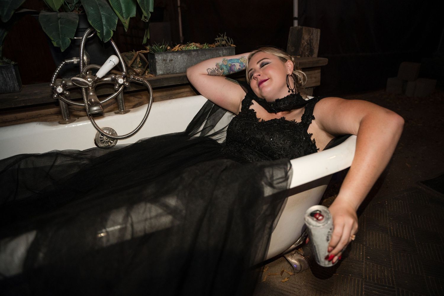 Person in a black dress reclining dramatically in a vintage-style bathtub during an event.