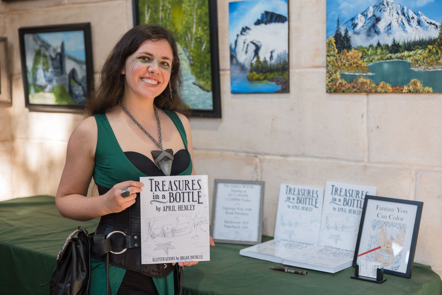 A vendor displays books and artwork at a Renaissance festival booth.