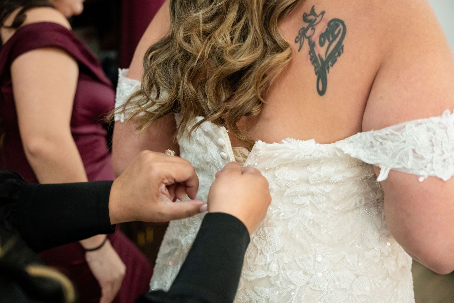 Detailed view of someone helping button up the back of an intricate lace wedding dress.