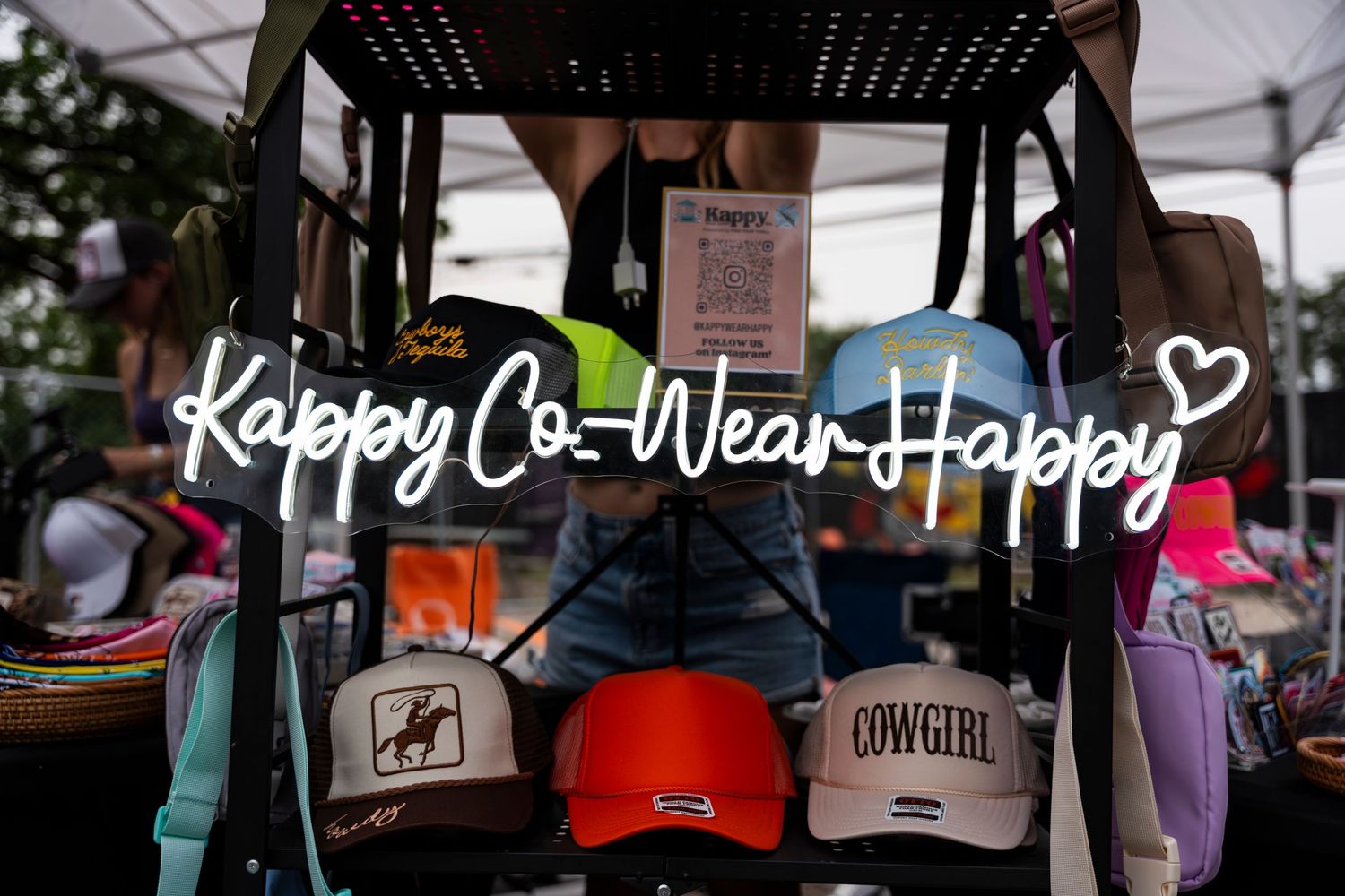 Collection of colorful hats and merchandise displayed under a 'Happy Co-Wear Happy' sign at a retail booth.