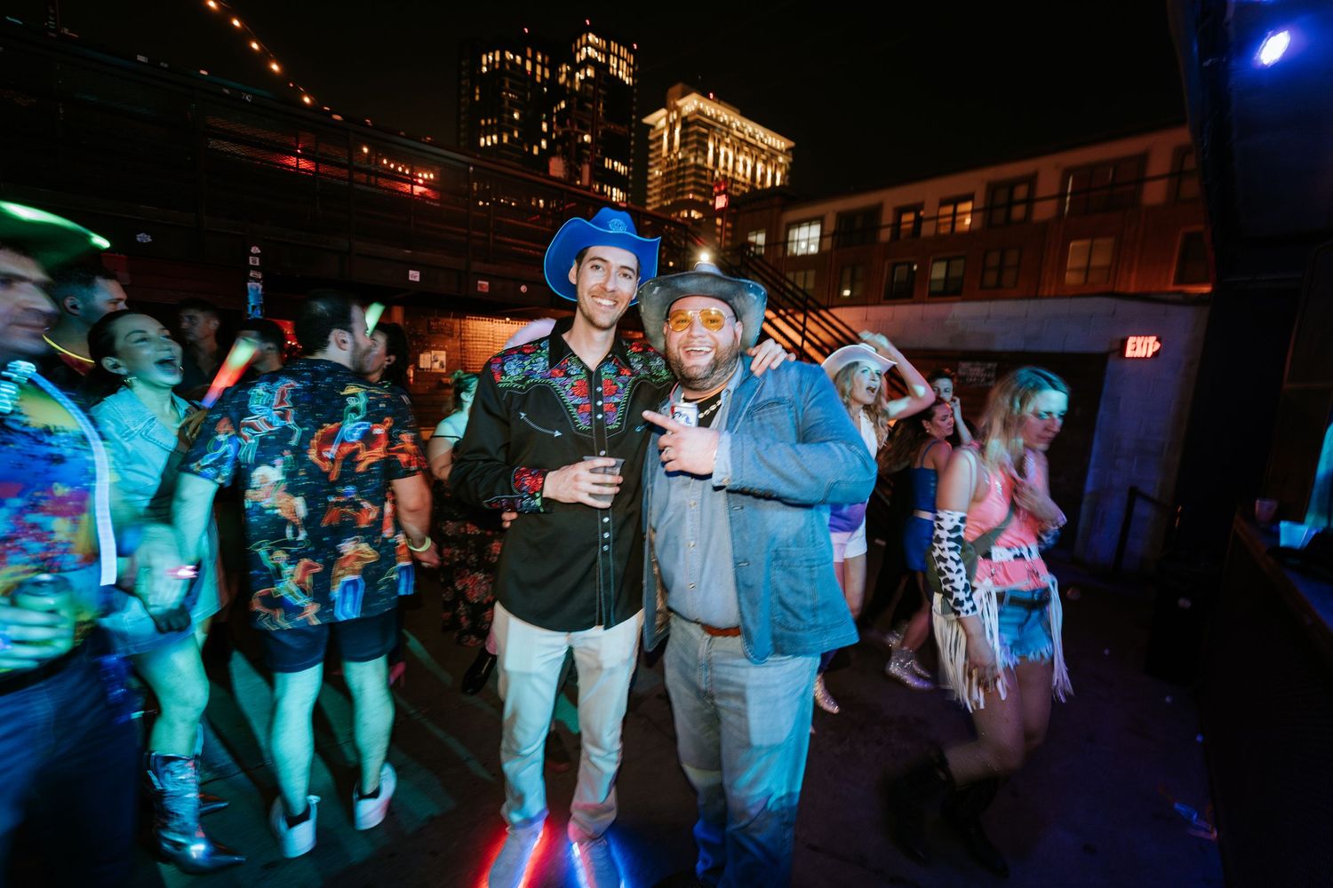 Nighttime rooftop party with city buildings in background and blue lighting.