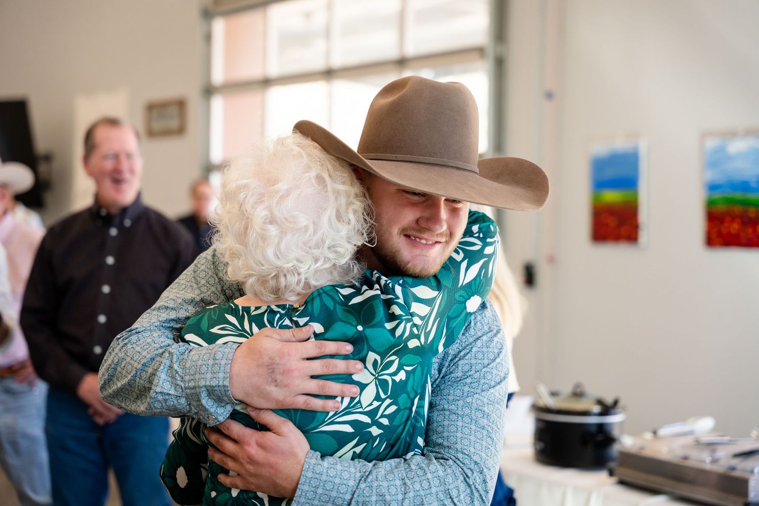 A warm embrace between two people, one wearing a cowboy hat and another in a green floral dress.