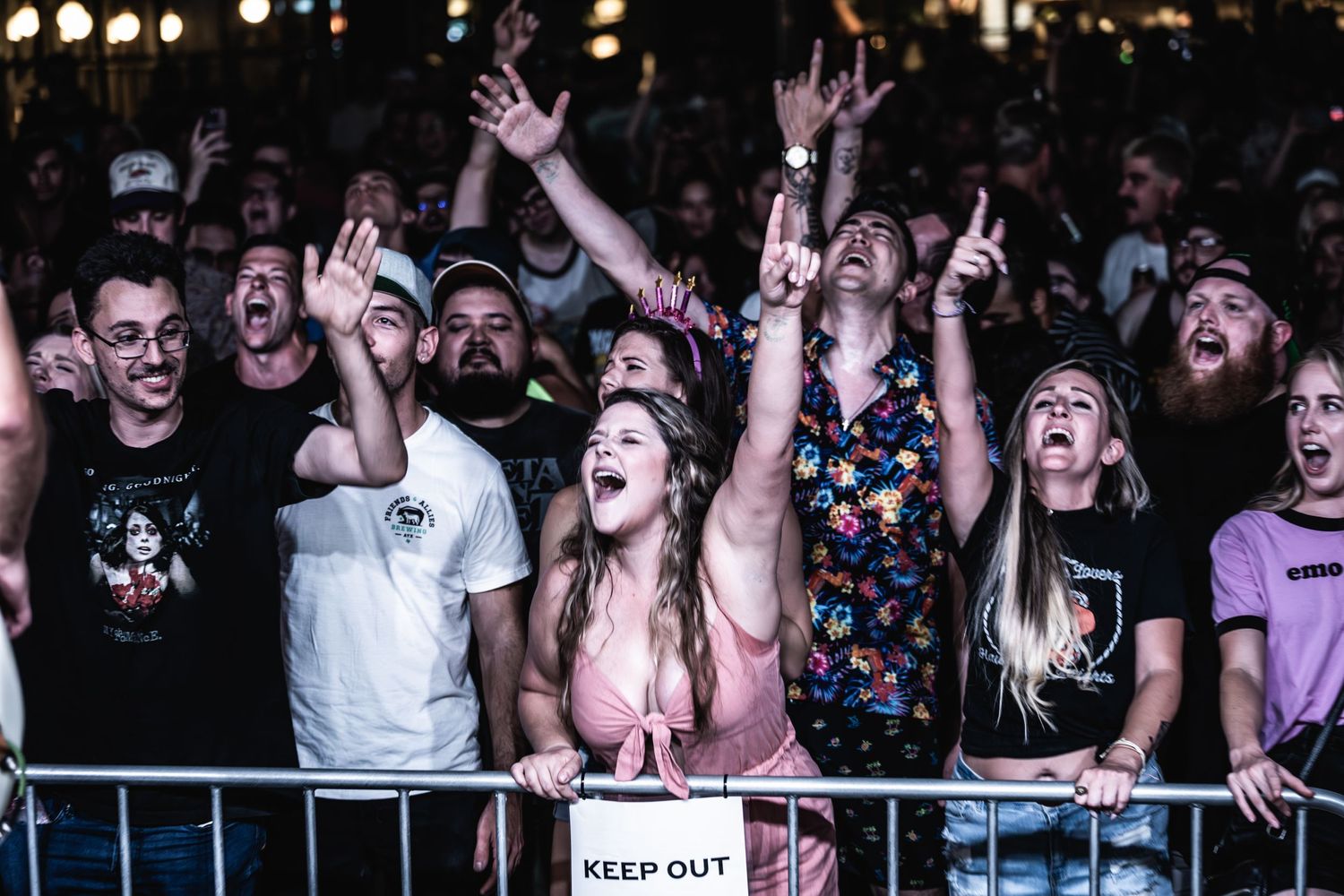 Enthusiastic concert crowd behind barrier reacting with excitement to live music performance.