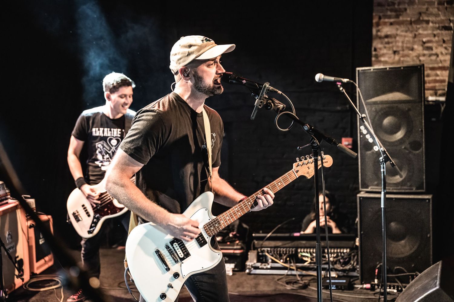 Musicians performing on brick-walled stage with guitar and bass during live concert.