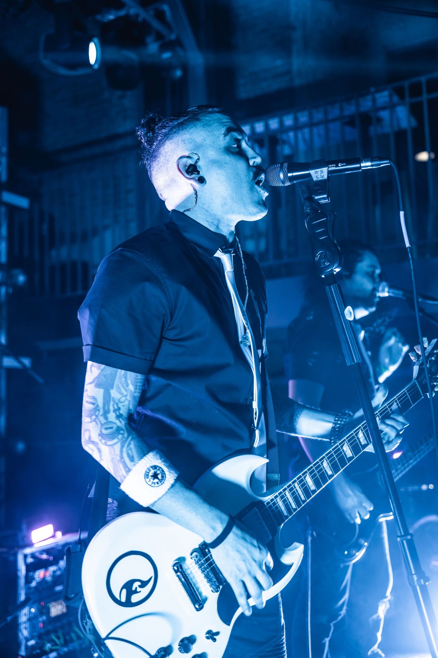 Guitarist performing on stage with white guitar under dramatic blue lighting.