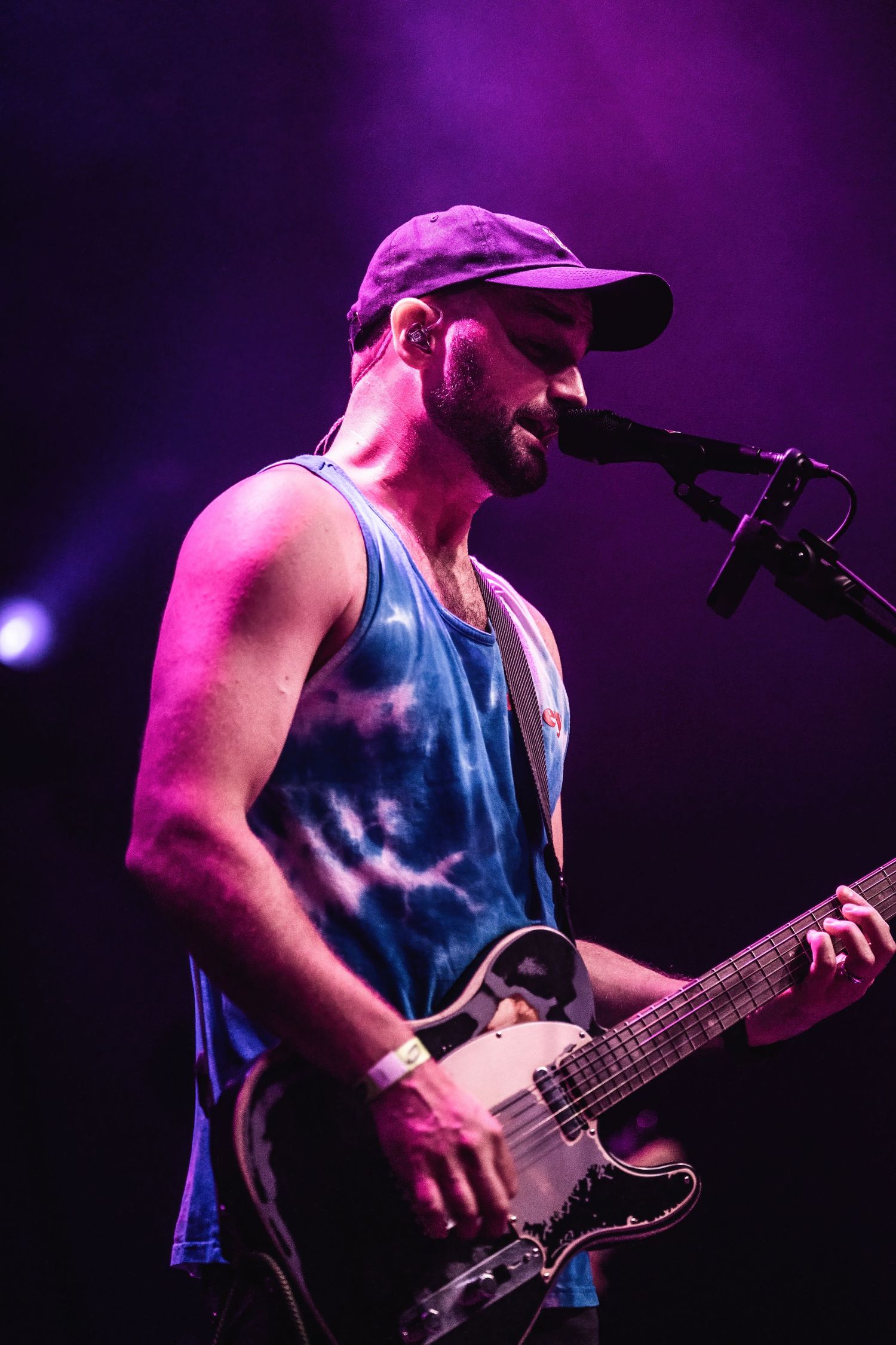 Musician plays guitar while singing into microphone under purple stage lighting.