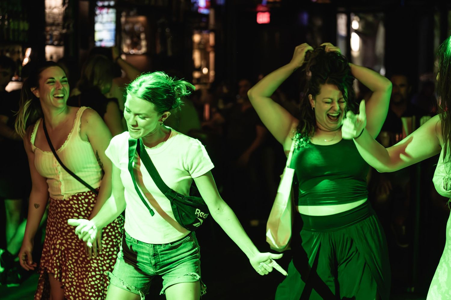 Crowd of concert attendees dancing energetically under green venue lighting.