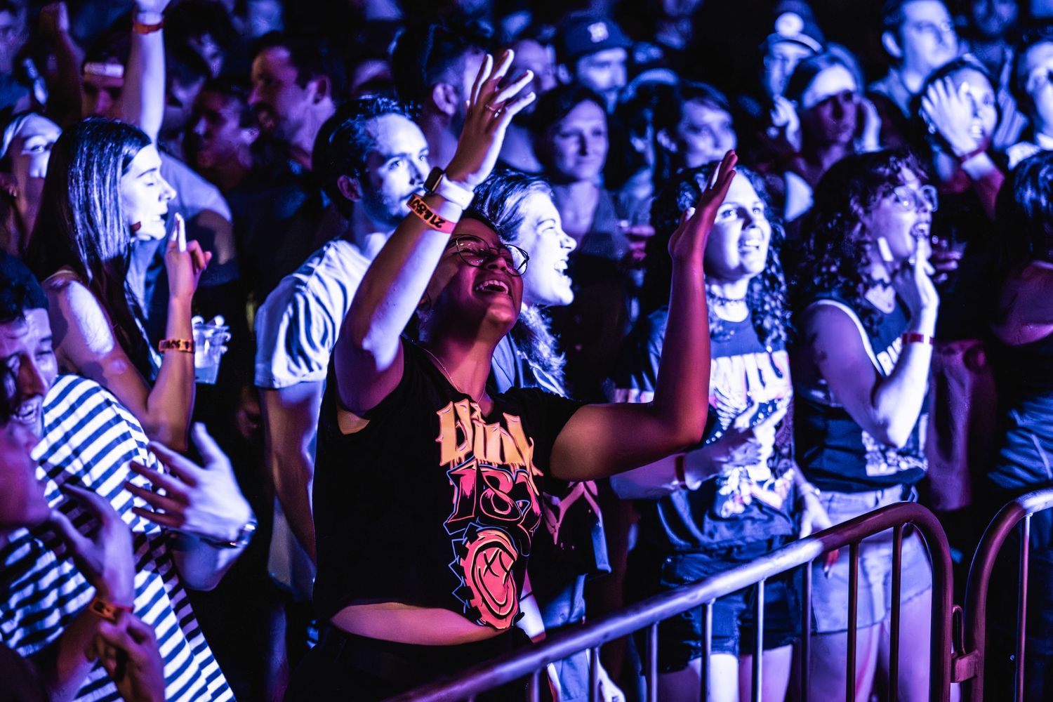 Enthusiastic concert crowd members raise hands and dance during live music performance.
